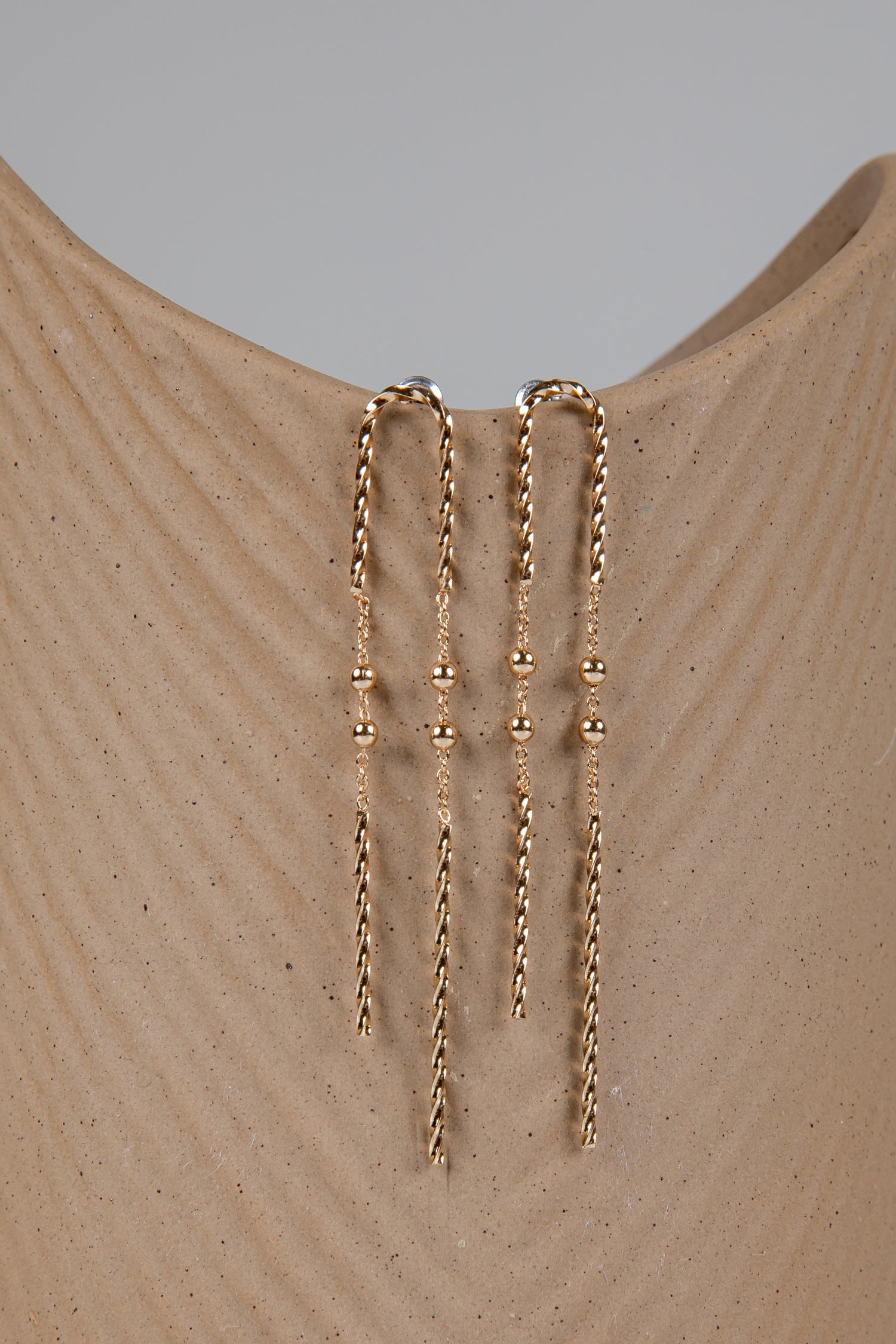 Gold chain earrings on a beige mannequin with a gray background