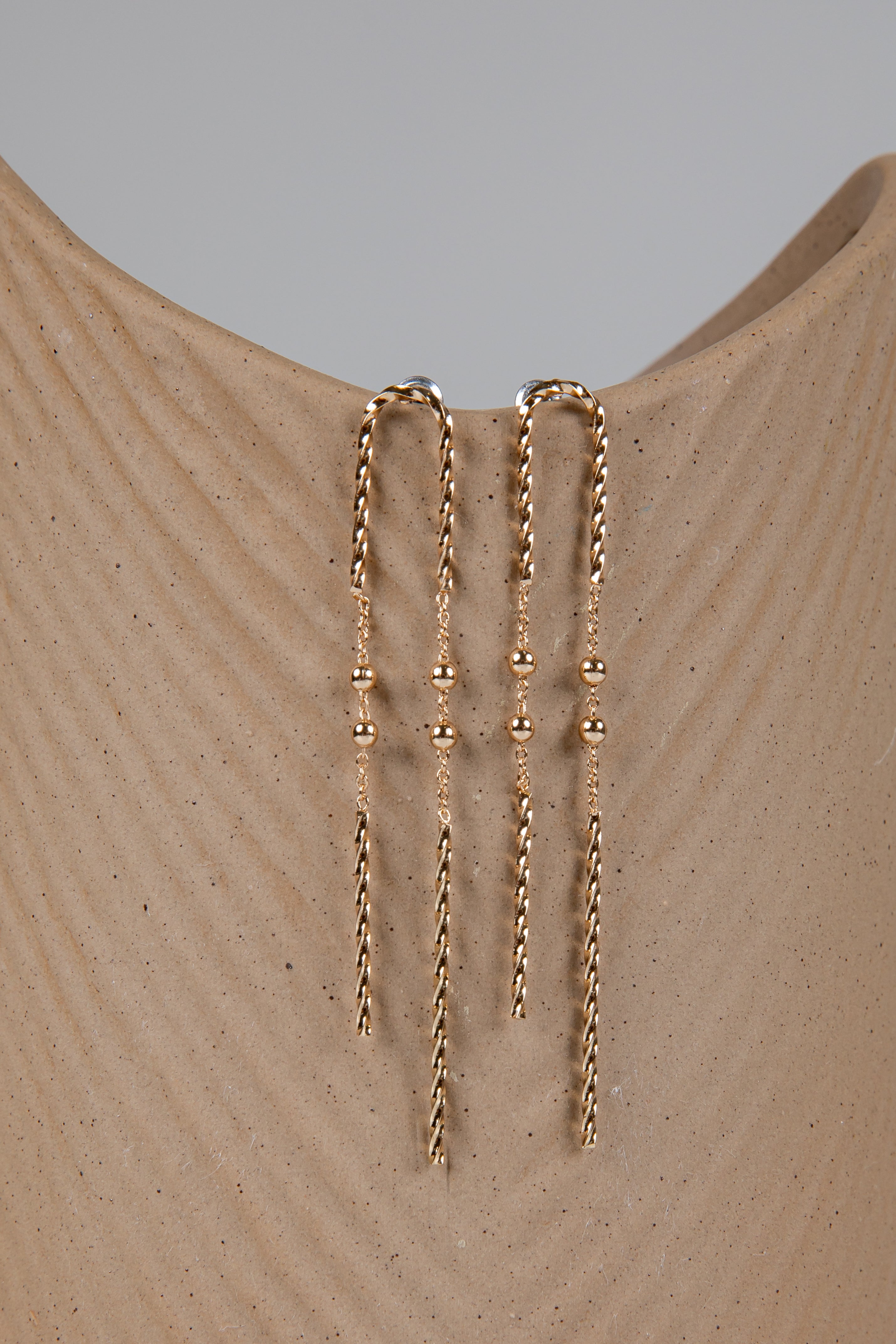 Gold chain earrings on a beige mannequin with a gray background