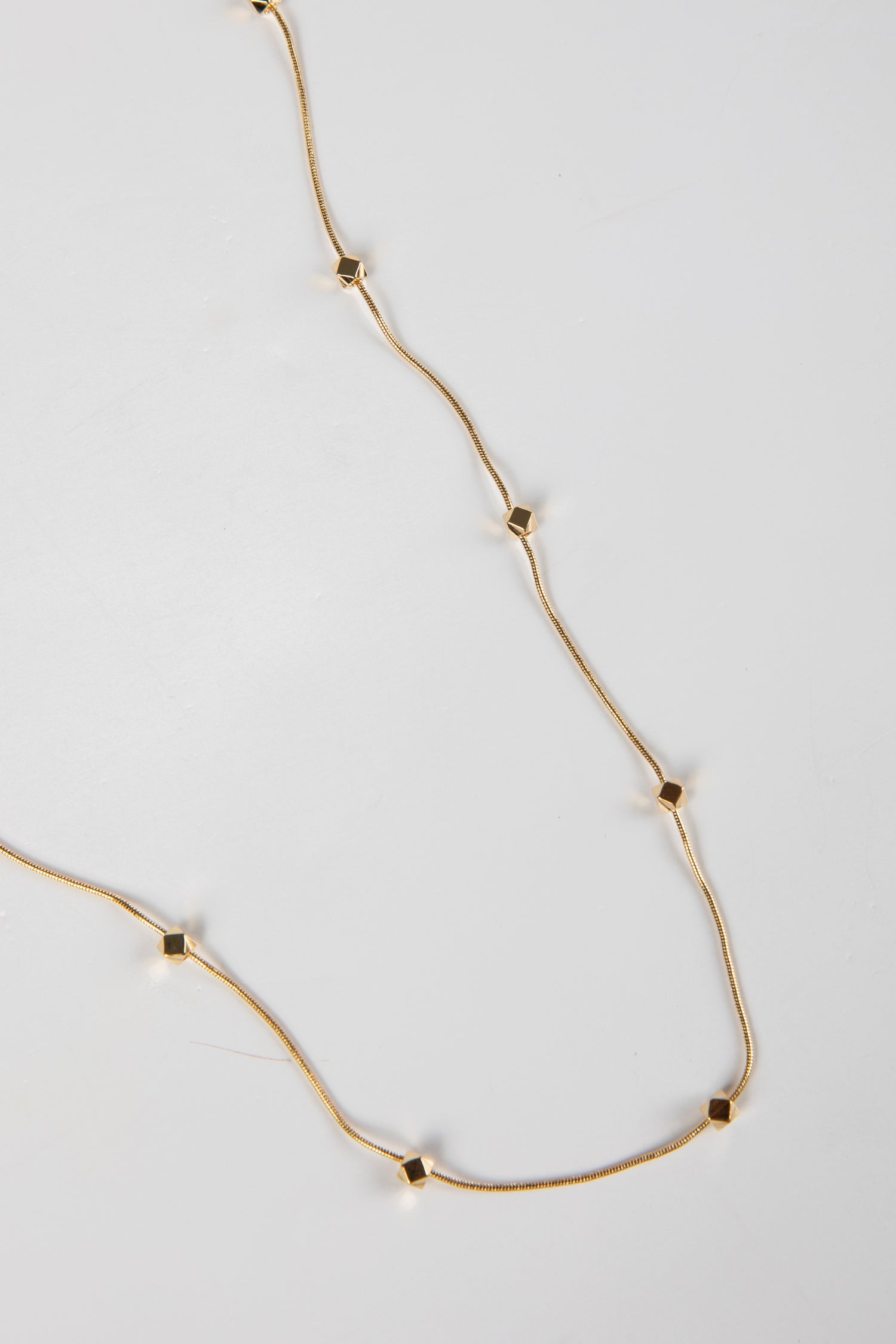 Gold necklace with small square pendants on a light gray background