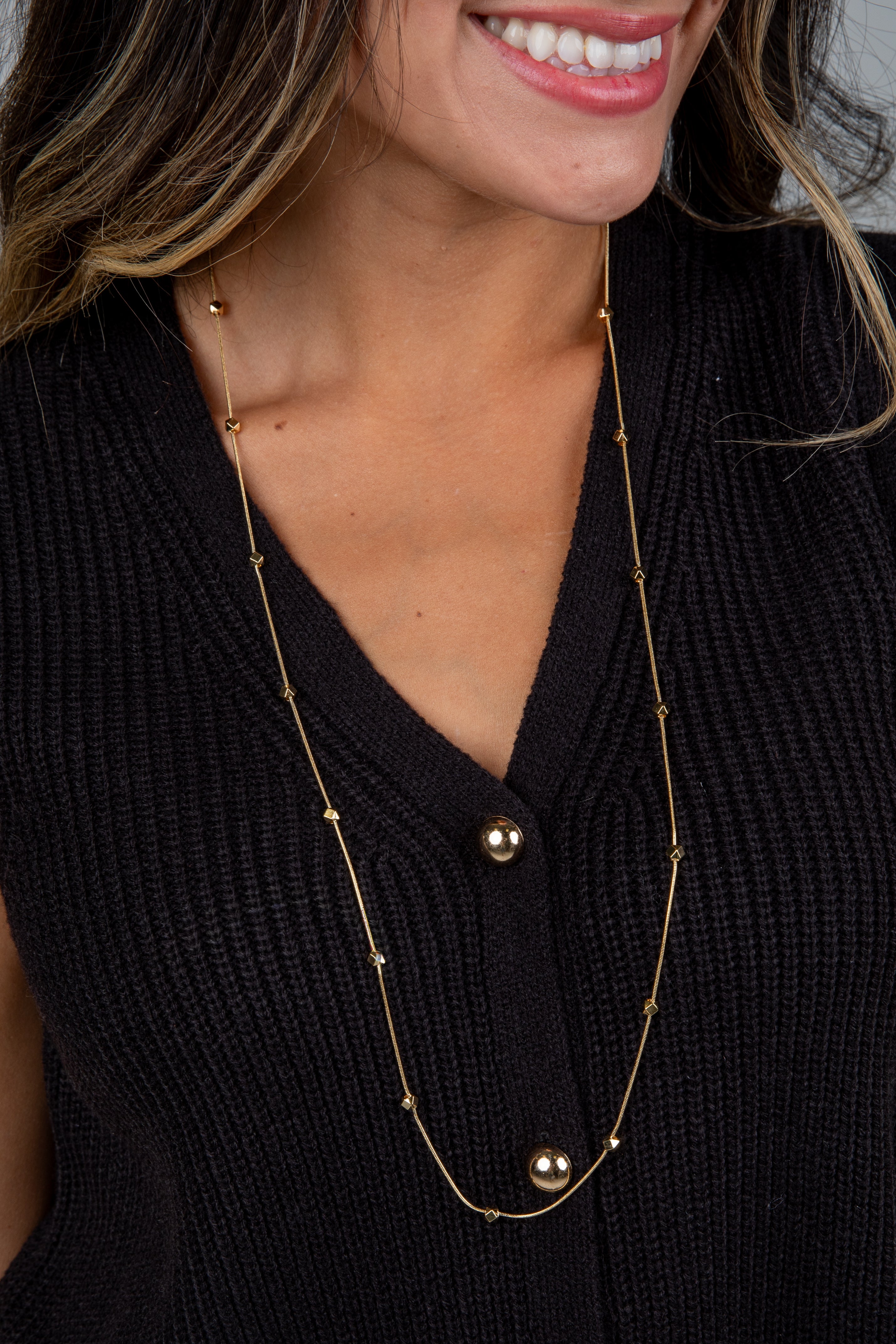 Woman wearing a long gold necklace with a black top