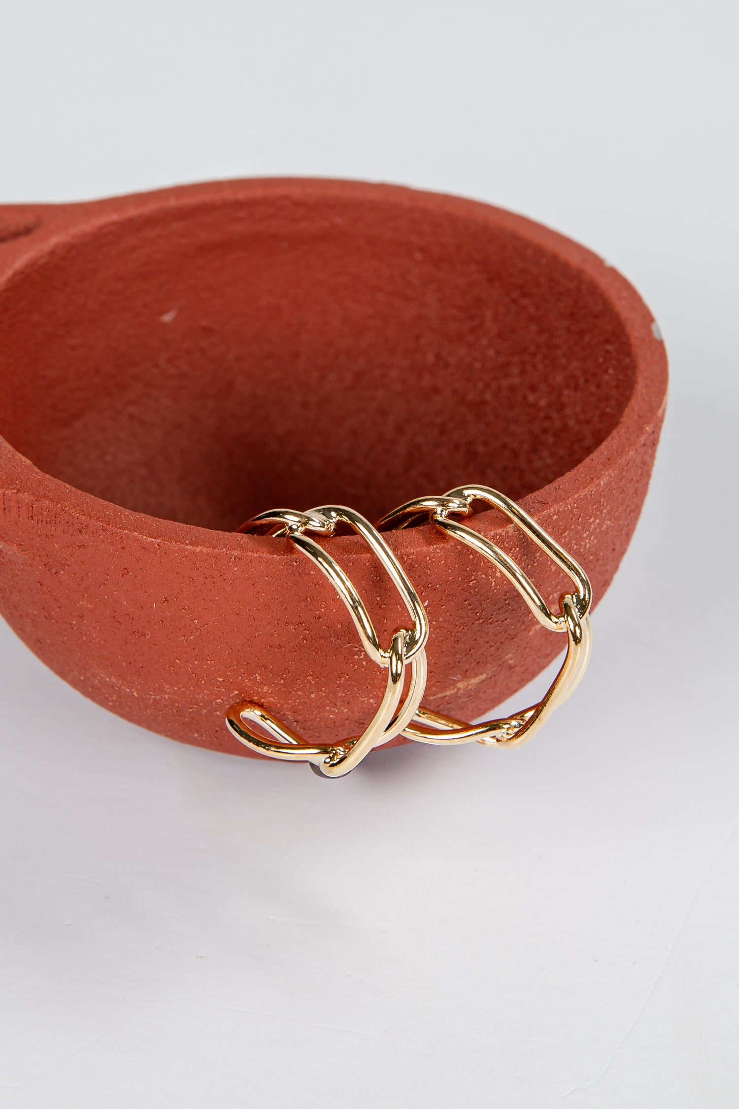 Gold chain bracelet on a terracotta bowl against a white background