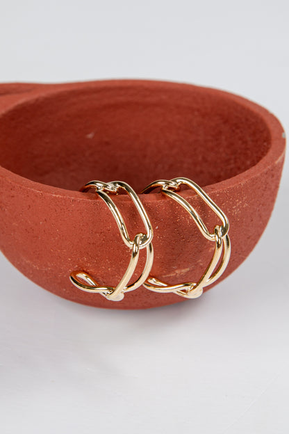 Three gold hoop earrings on a terracotta dish against a white background