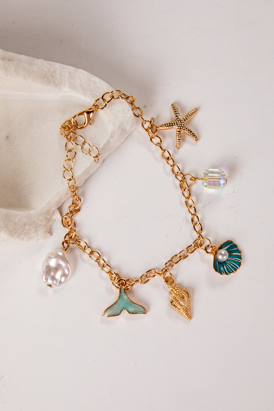 Gold bracelet with various charms including a starfish, shell, and mermaid tail on a white background.