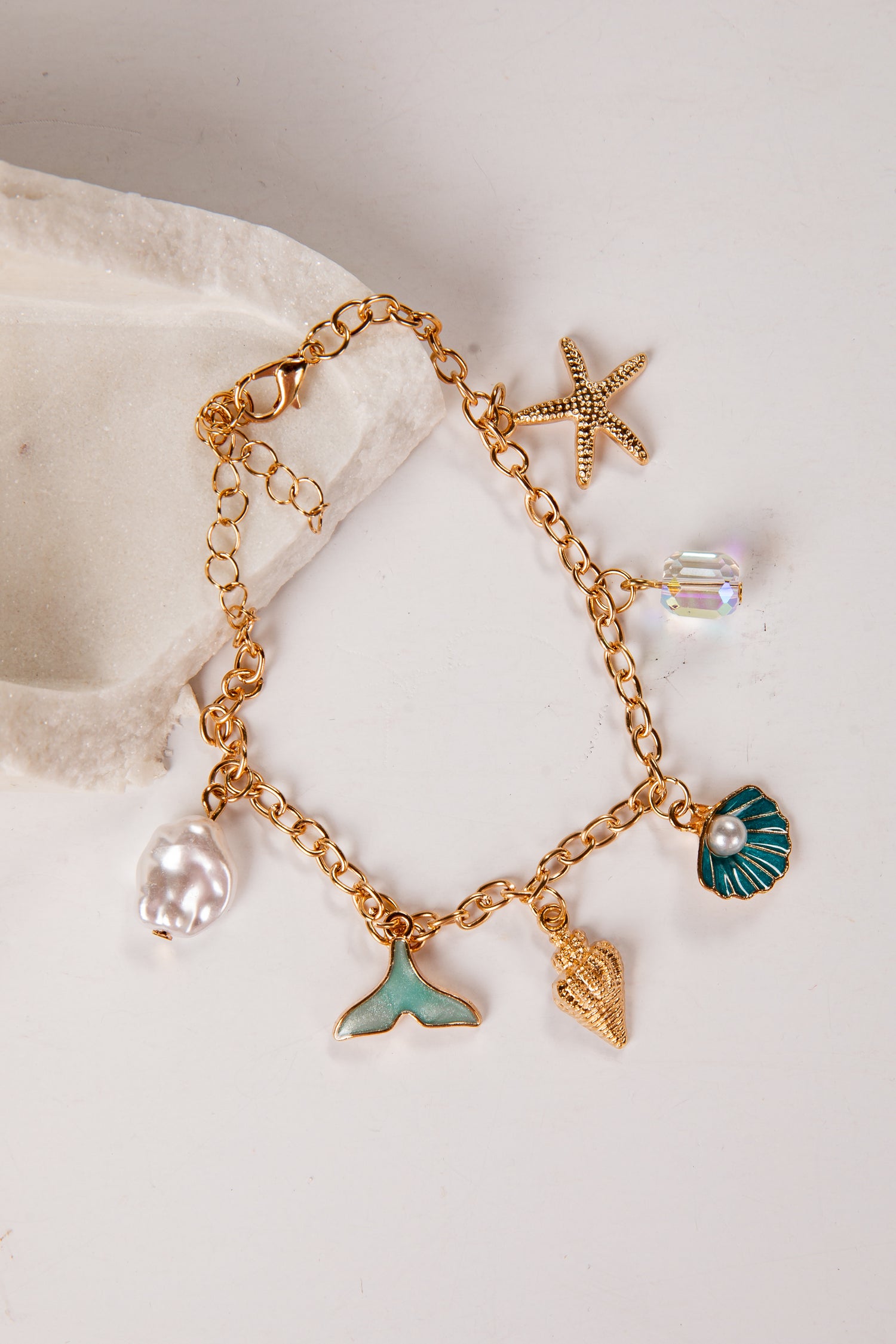 Gold bracelet with various charms including a starfish, shell, and mermaid tail on a white background.