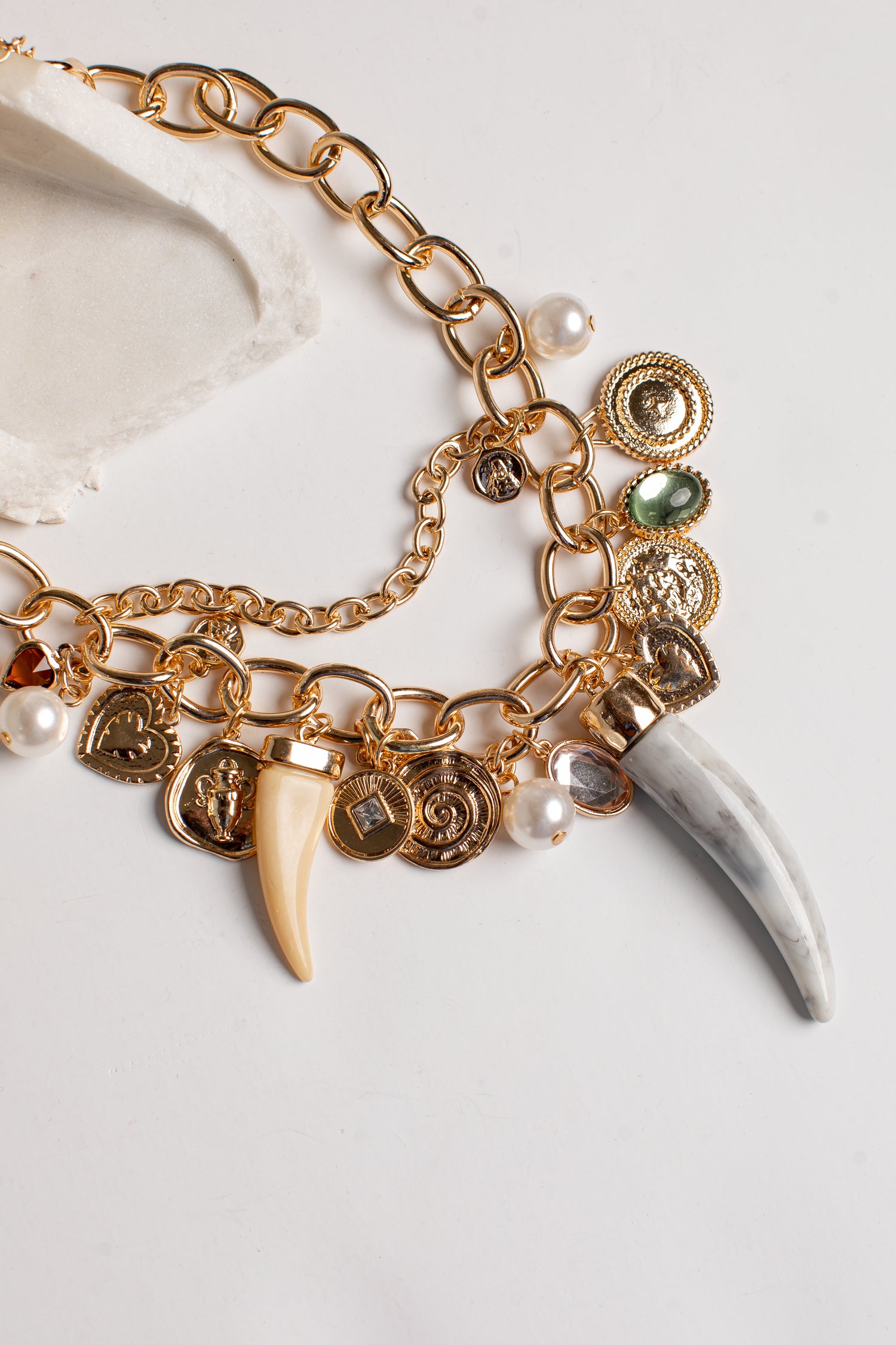 Gold-tone charm bracelet featuring a chunky chain, multiple coin charms, a cream-colored tooth, a white bone fragment, and small pearl beads on a light background.