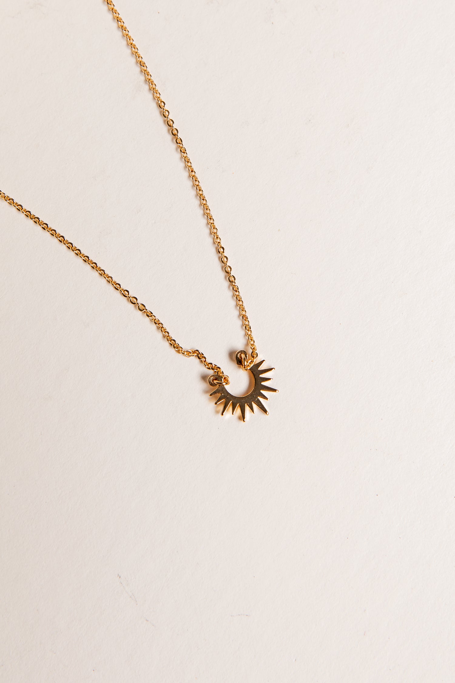 Gold necklace with a sun-shaped pendant on a light beige background