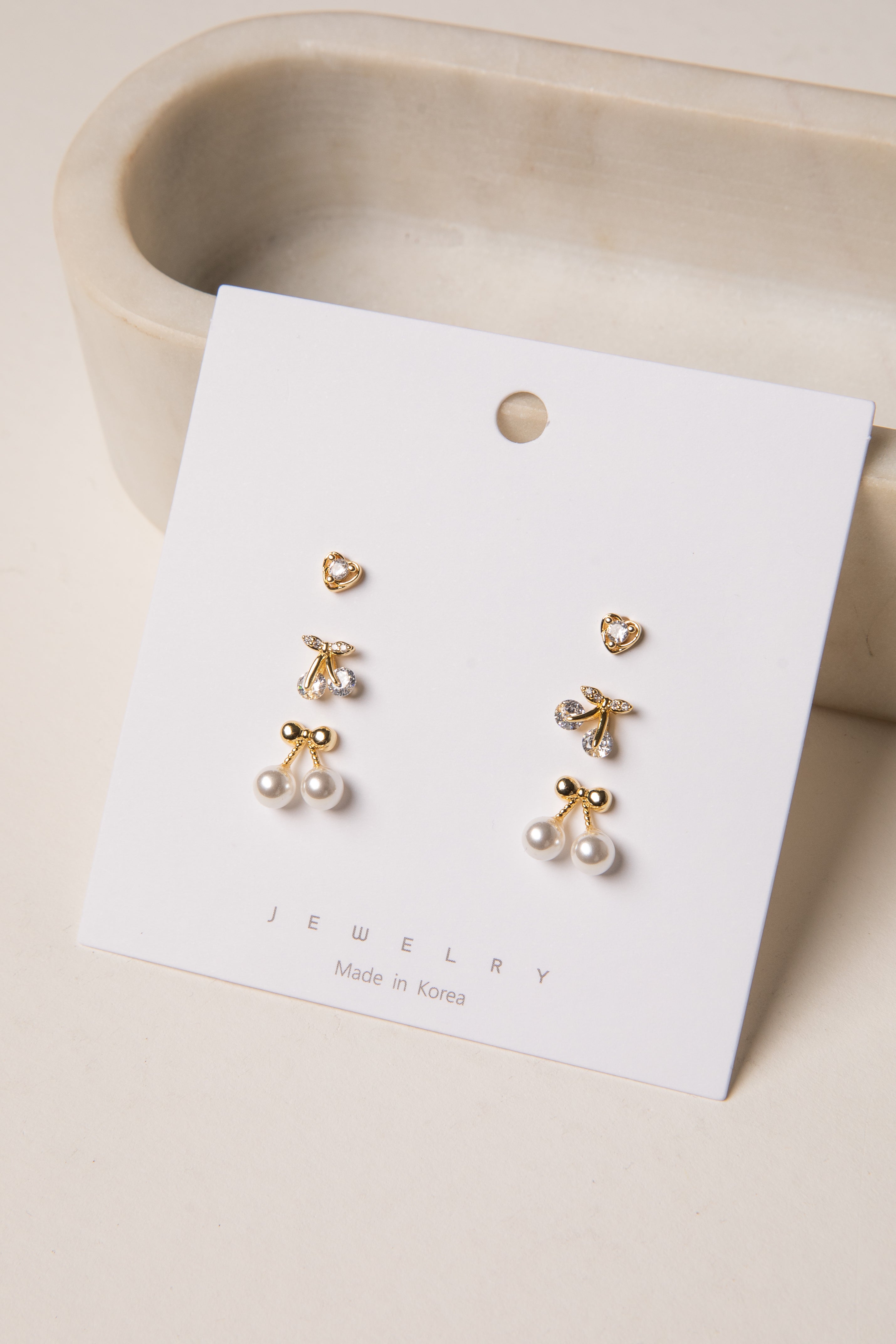Pair of gold and pearl earrings on a jewelry card with a beige background