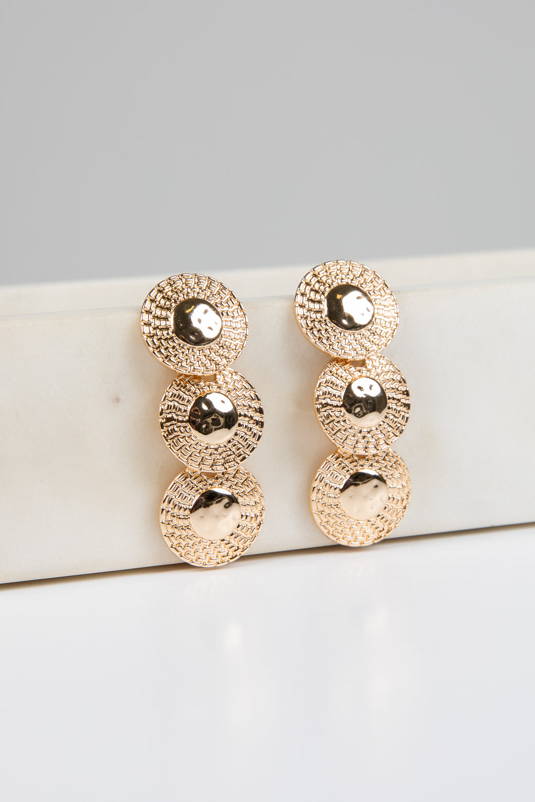 Gold earrings on a white surface with a gray background