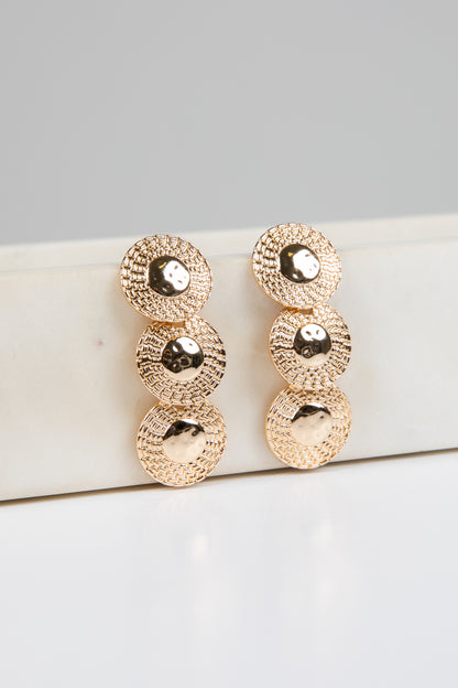 Gold earrings on a white surface with a gray background