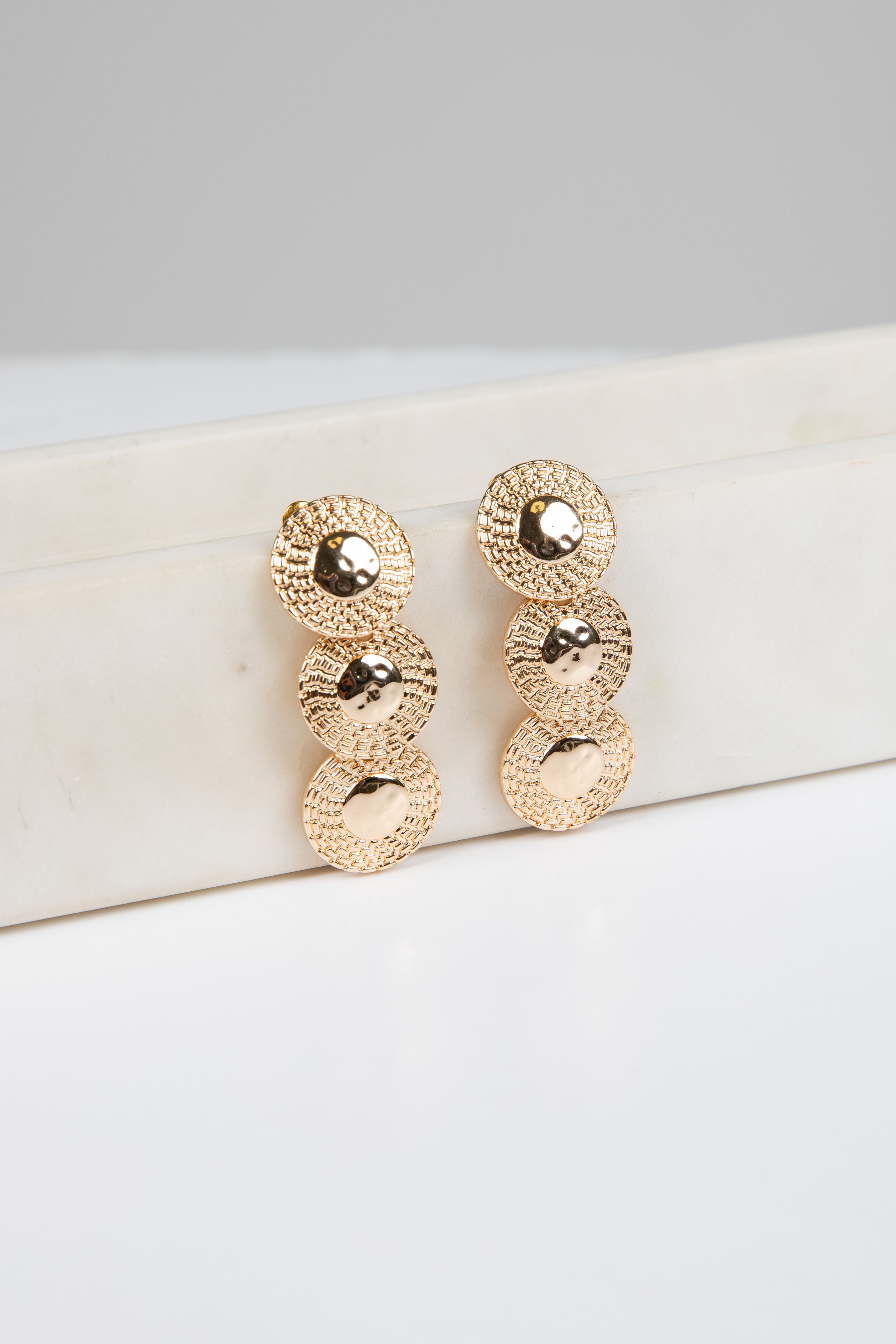 Rose gold earrings on a white surface with a gray background