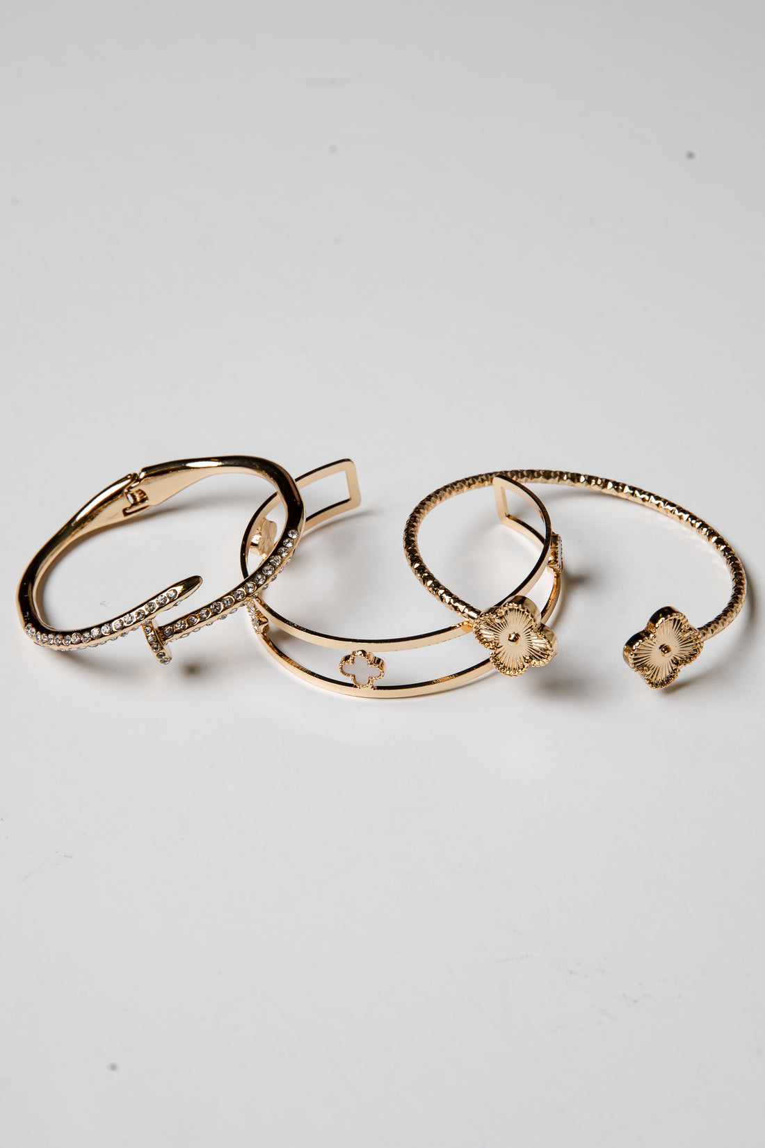 Three gold bracelets with floral designs on a light gray background