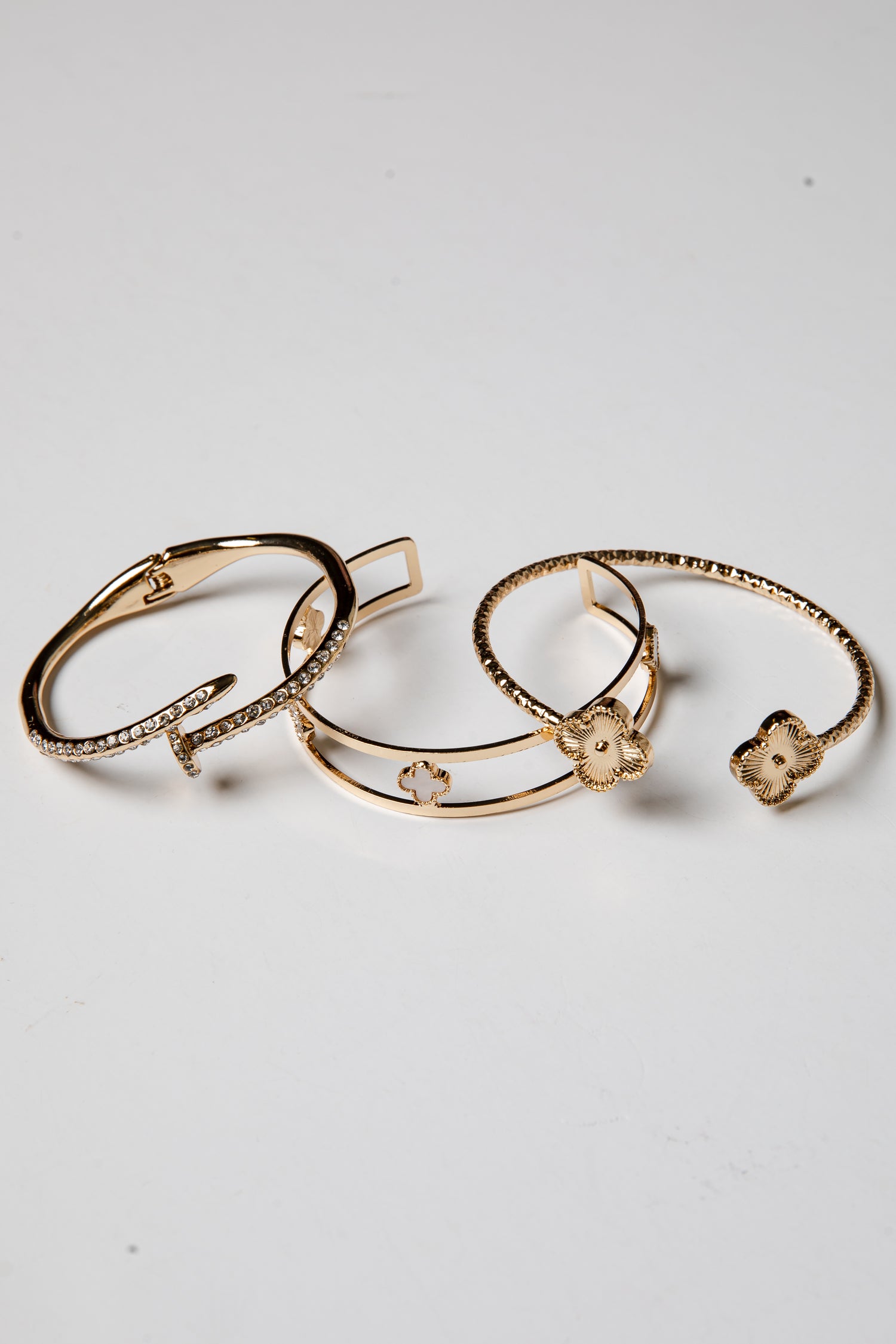 Three gold bracelets with floral designs on a light gray background