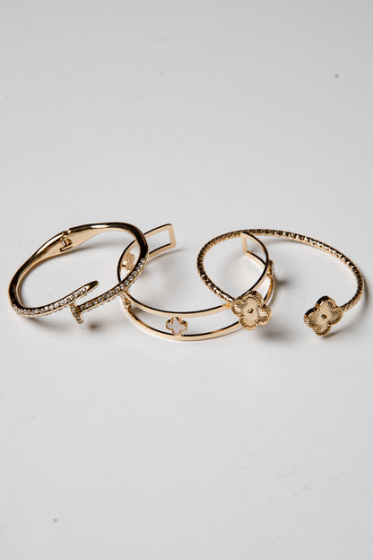 Three gold bracelets with floral designs on a light gray background