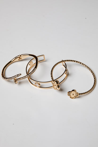 Three gold bracelets with intricate designs on a light gray background