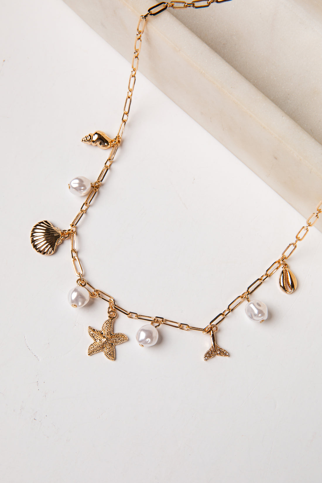 Gold necklace with starfish, shell, and pearl charms on a light background