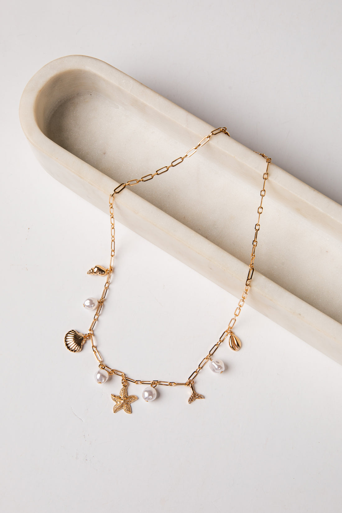 Gold anklet with various charms on a white surface