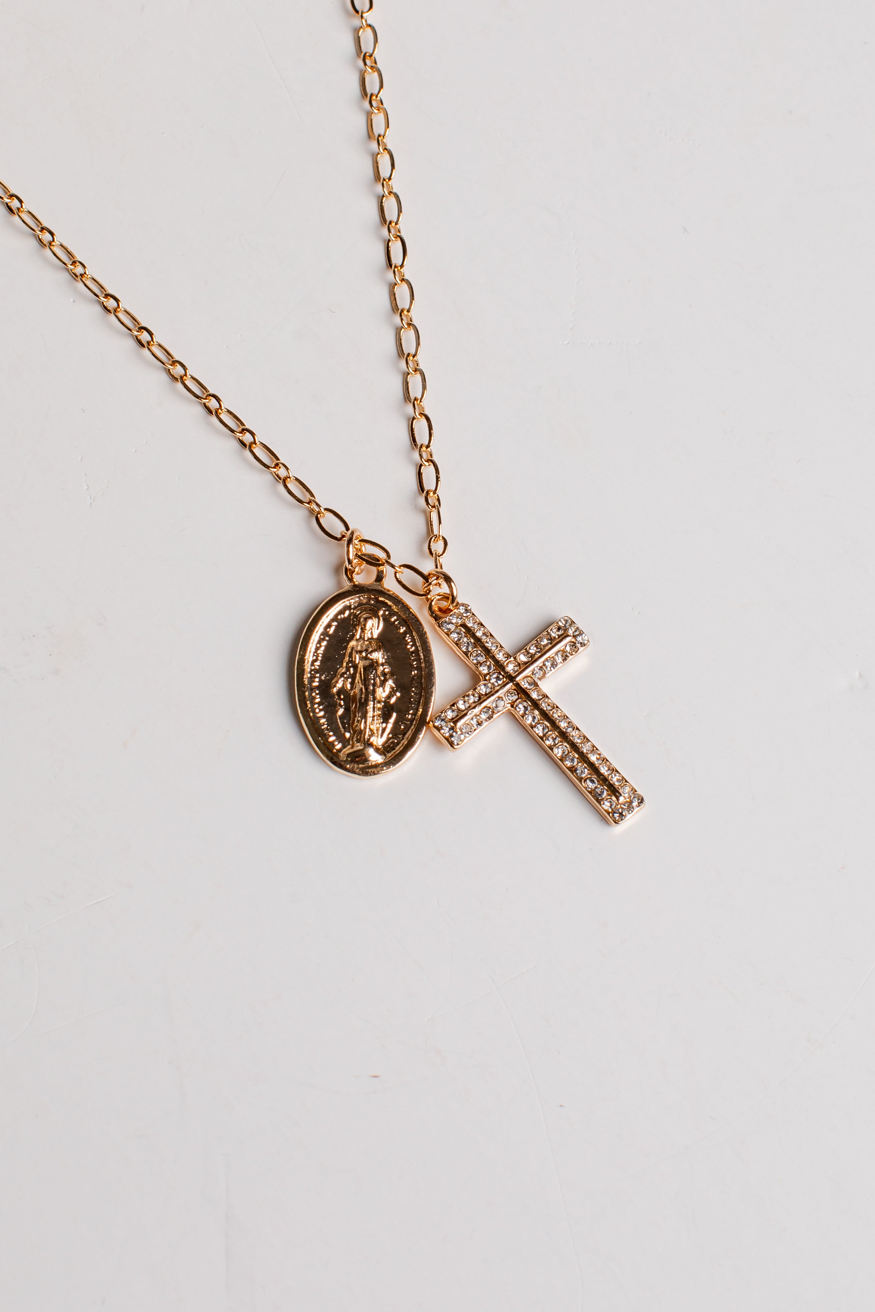 A rose gold chain necklace featuring two pendants: an oval Miraculous Medal pendant and a rectangular cross paved with small clear stones, displayed on a light gray background.