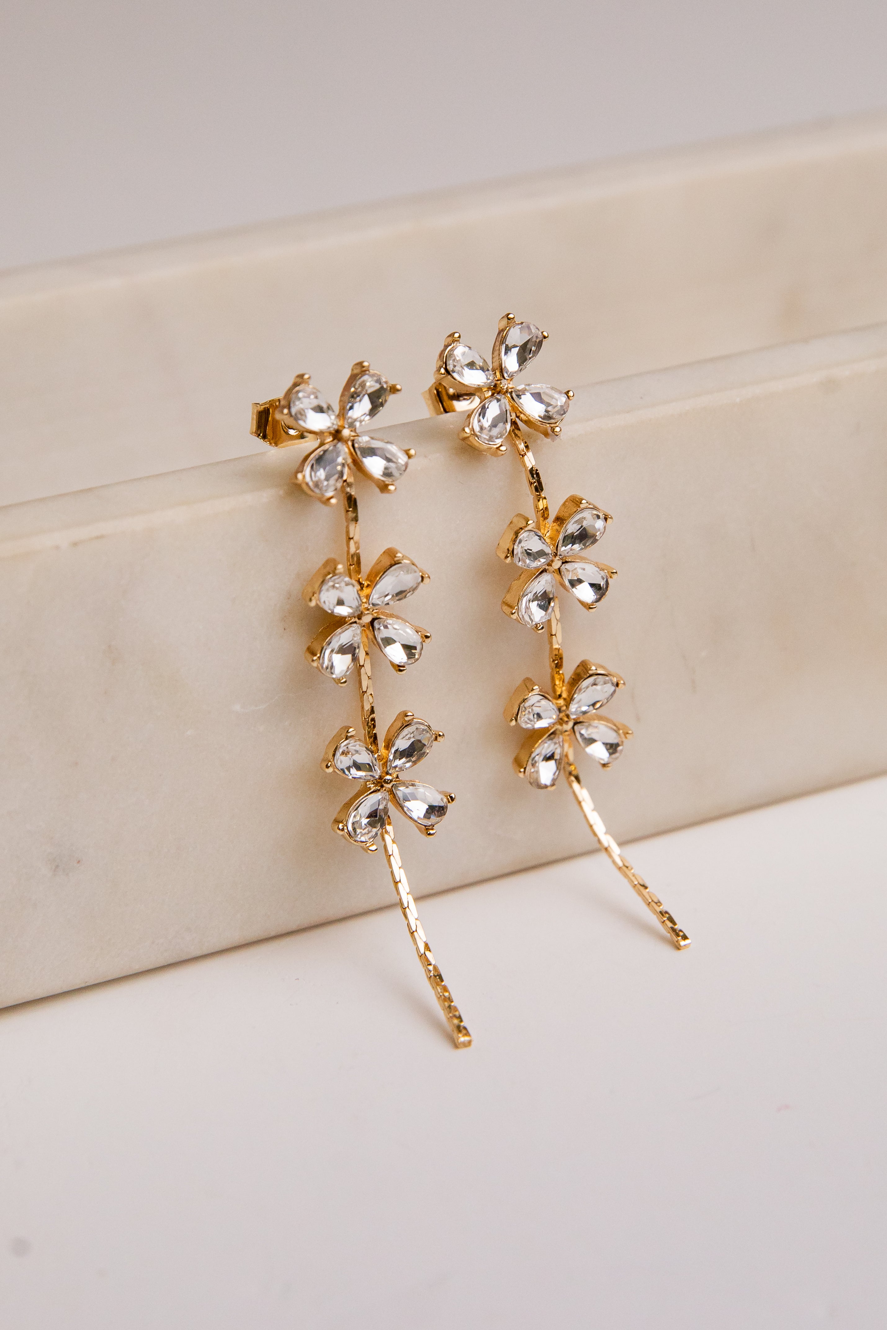 Gold floral earrings on a beige surface