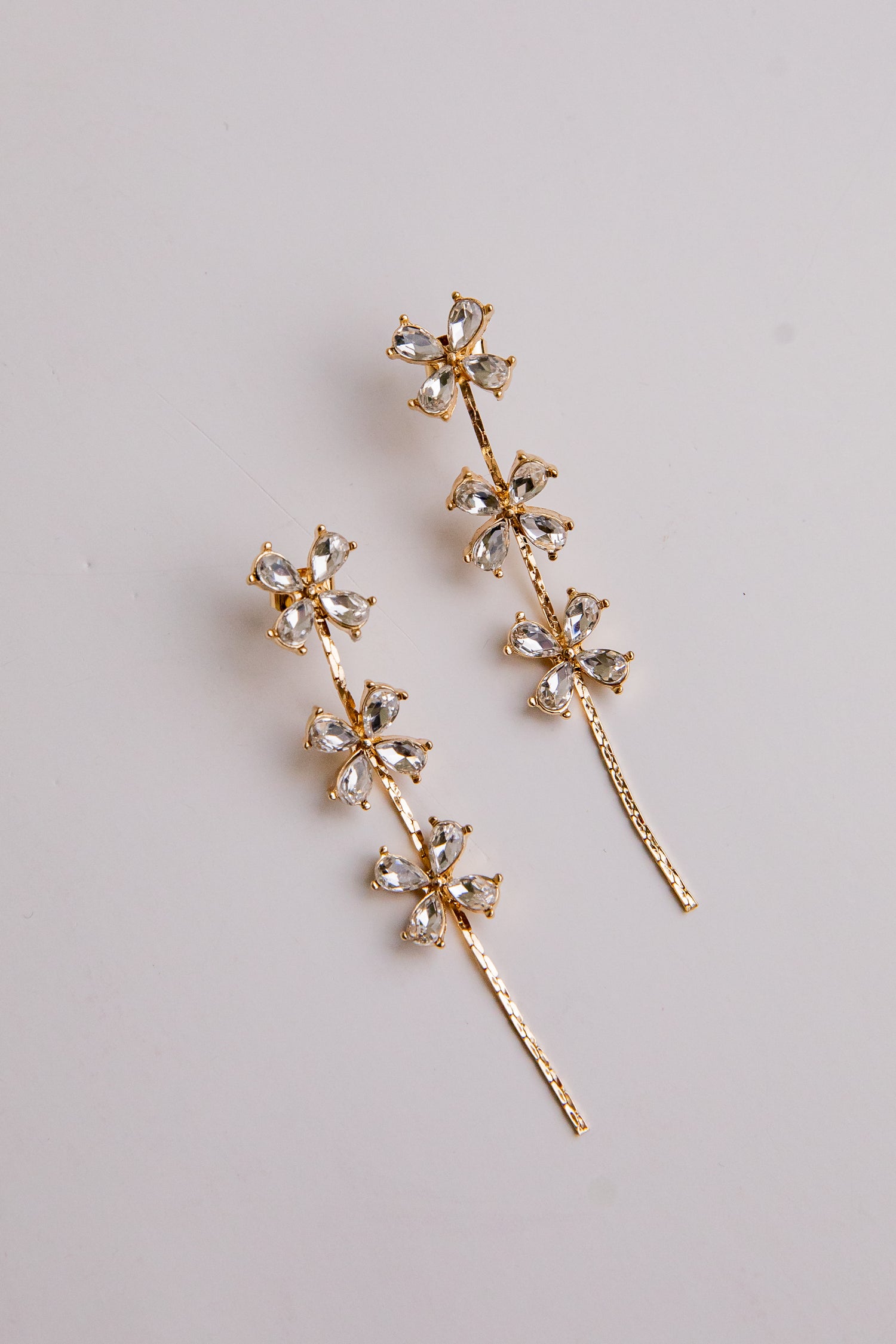 Gold floral earrings with clear gemstones on a light gray background