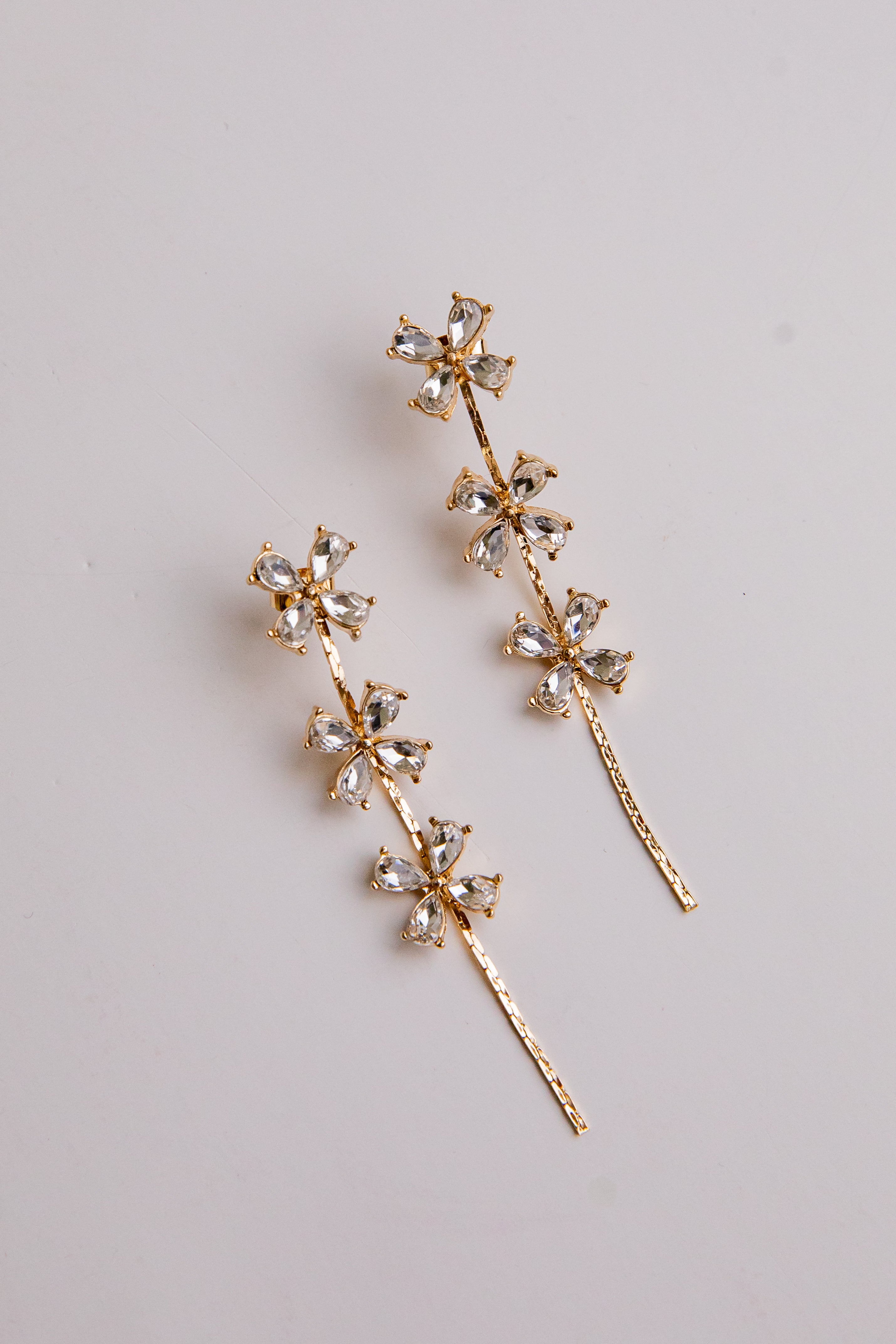 Gold floral earrings with clear gemstones on a light gray background