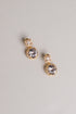 A pair of gold drop earrings with large clear round gemstones and smaller clear stones above them, photographed on a plain light gray background.