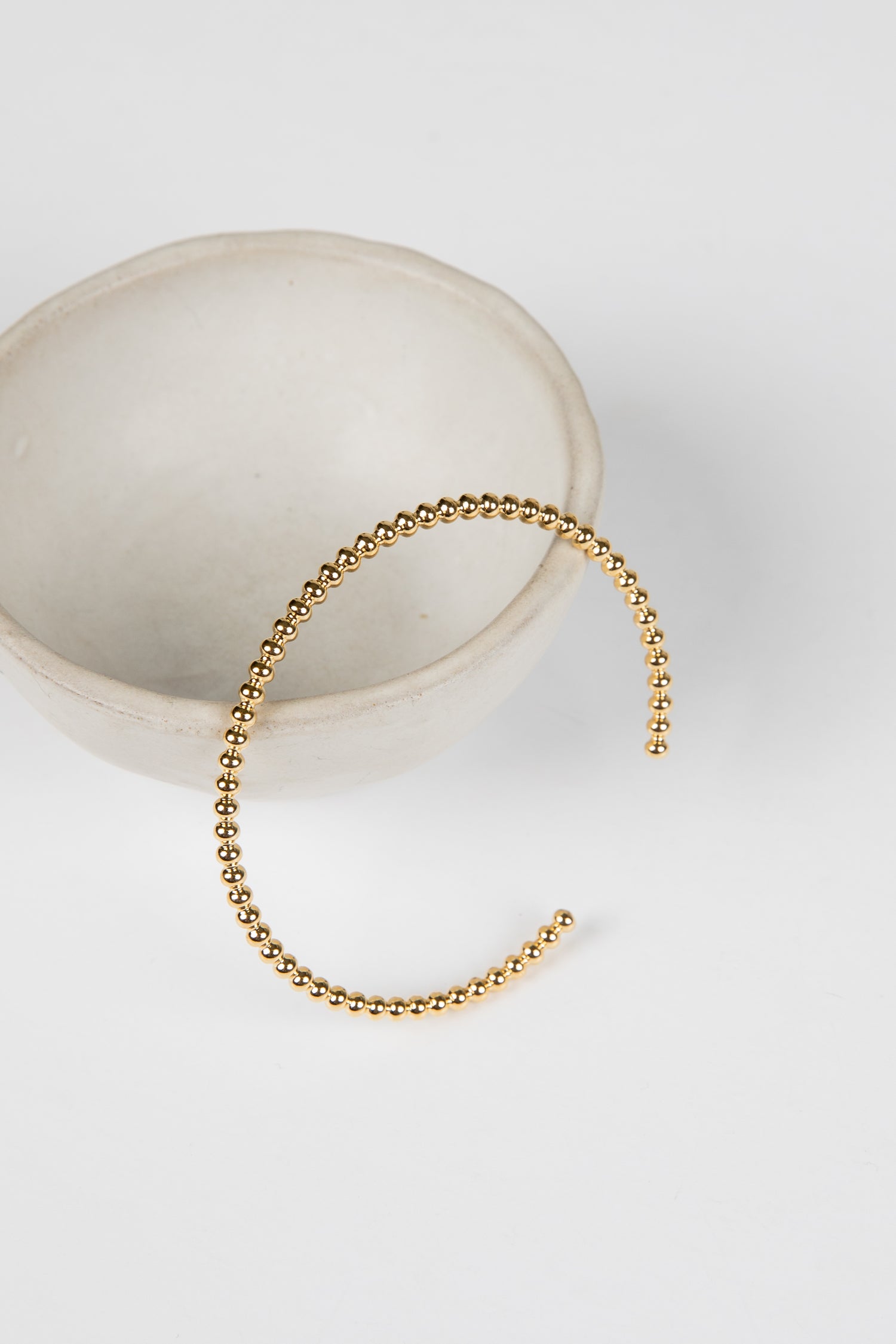 Gold beaded bracelet on a white surface with a neutral background