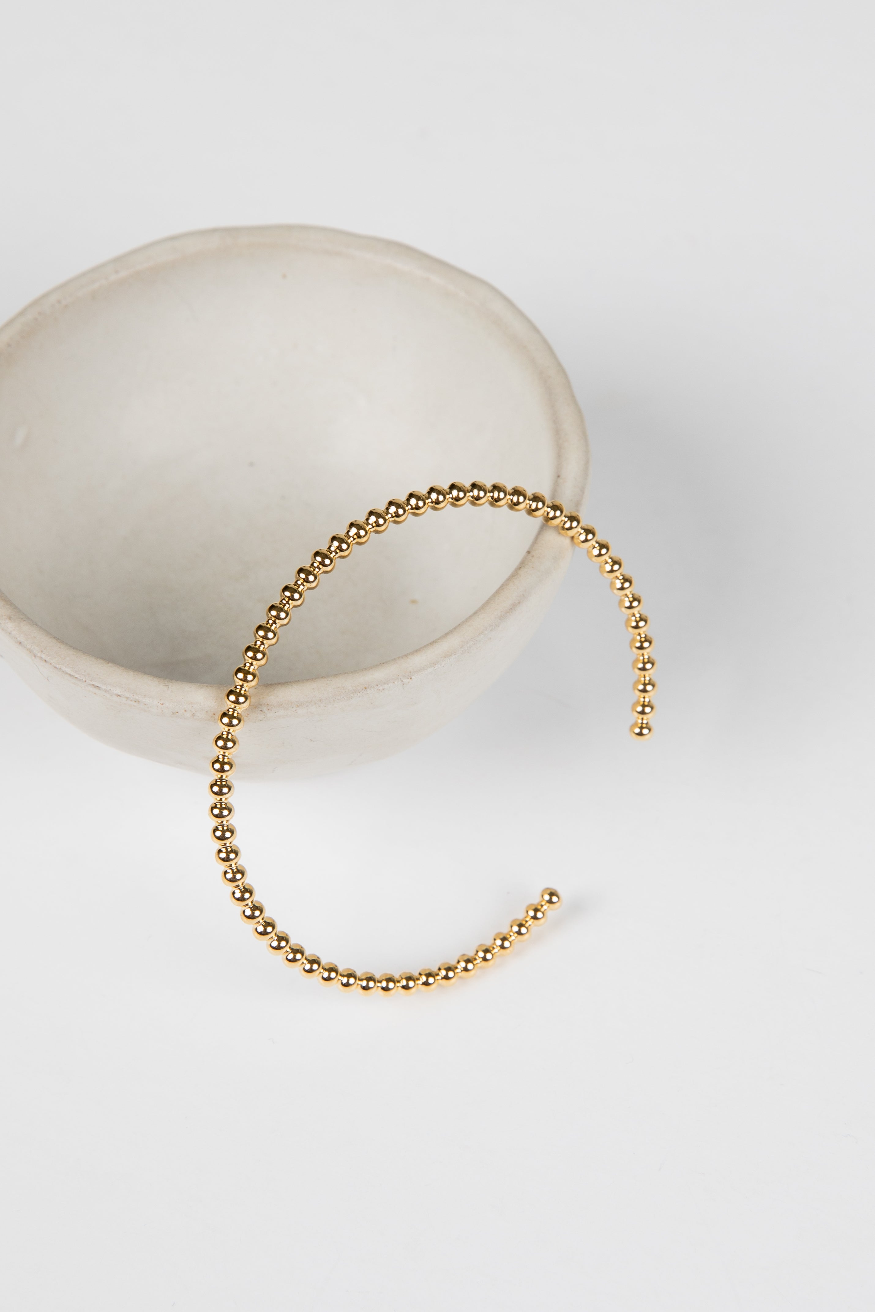 Gold beaded bracelet on a white surface with a neutral background