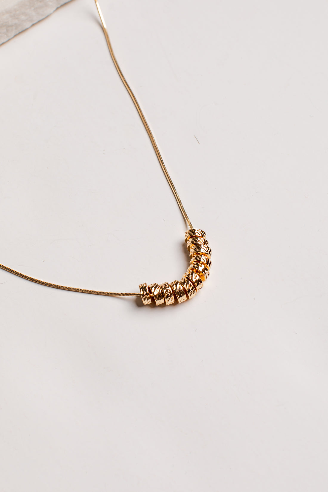 A delicate gold chain necklace featuring a curved segment of faceted, textured gold beads, photographed on a clean off-white surface.