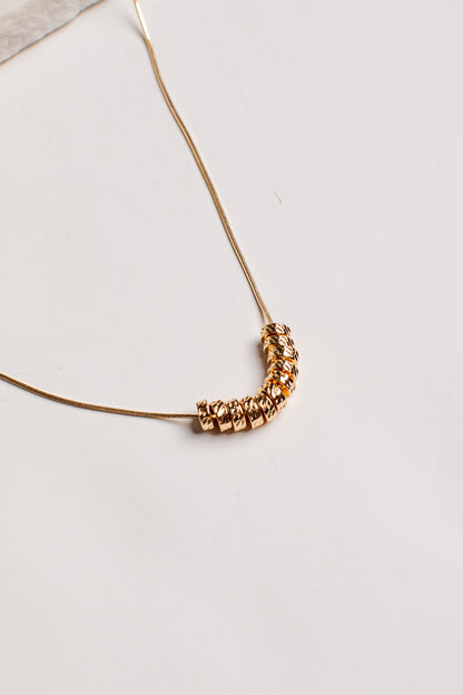 A delicate gold chain necklace featuring a curved segment of faceted, textured gold beads, photographed on a clean off-white surface.