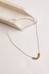 A delicate gold chain necklace with a small textured gold pendant, displayed on a light cream-colored stone riser against a clean white background.