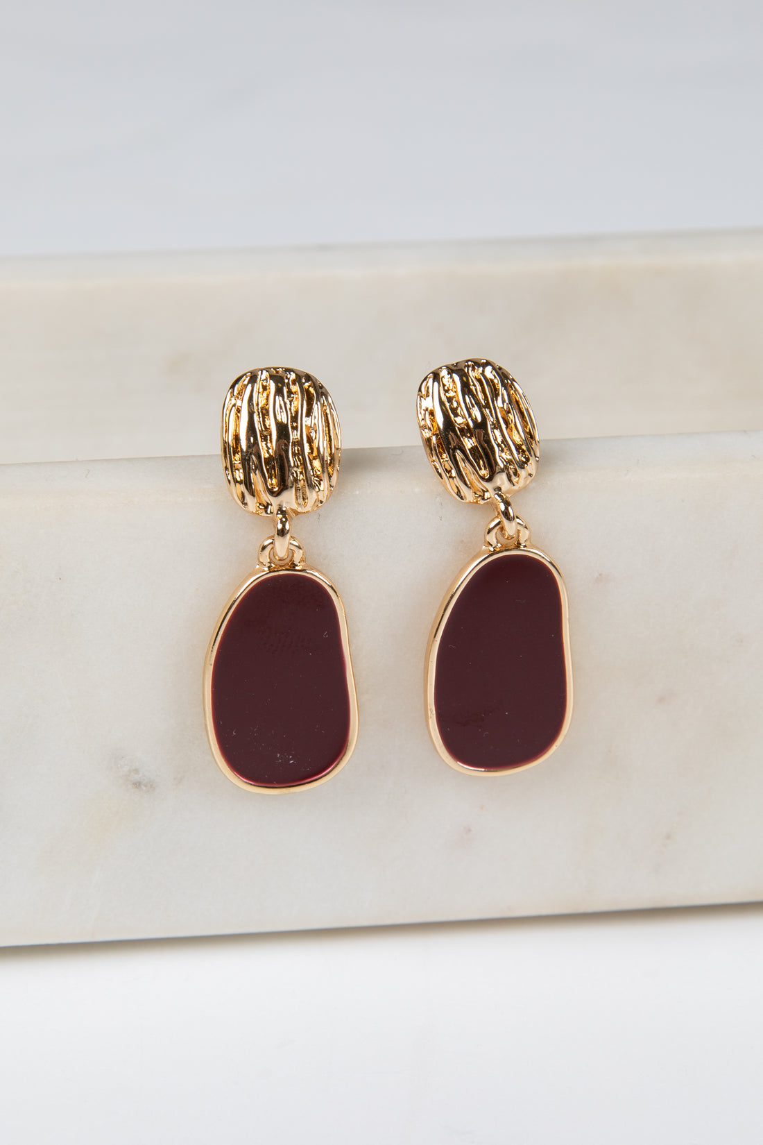 Gold and burgundy earrings on a marble surface