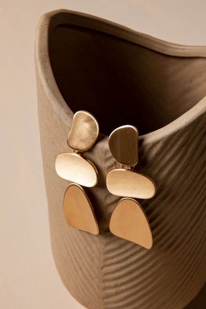 Gold earrings on a textured beige surface