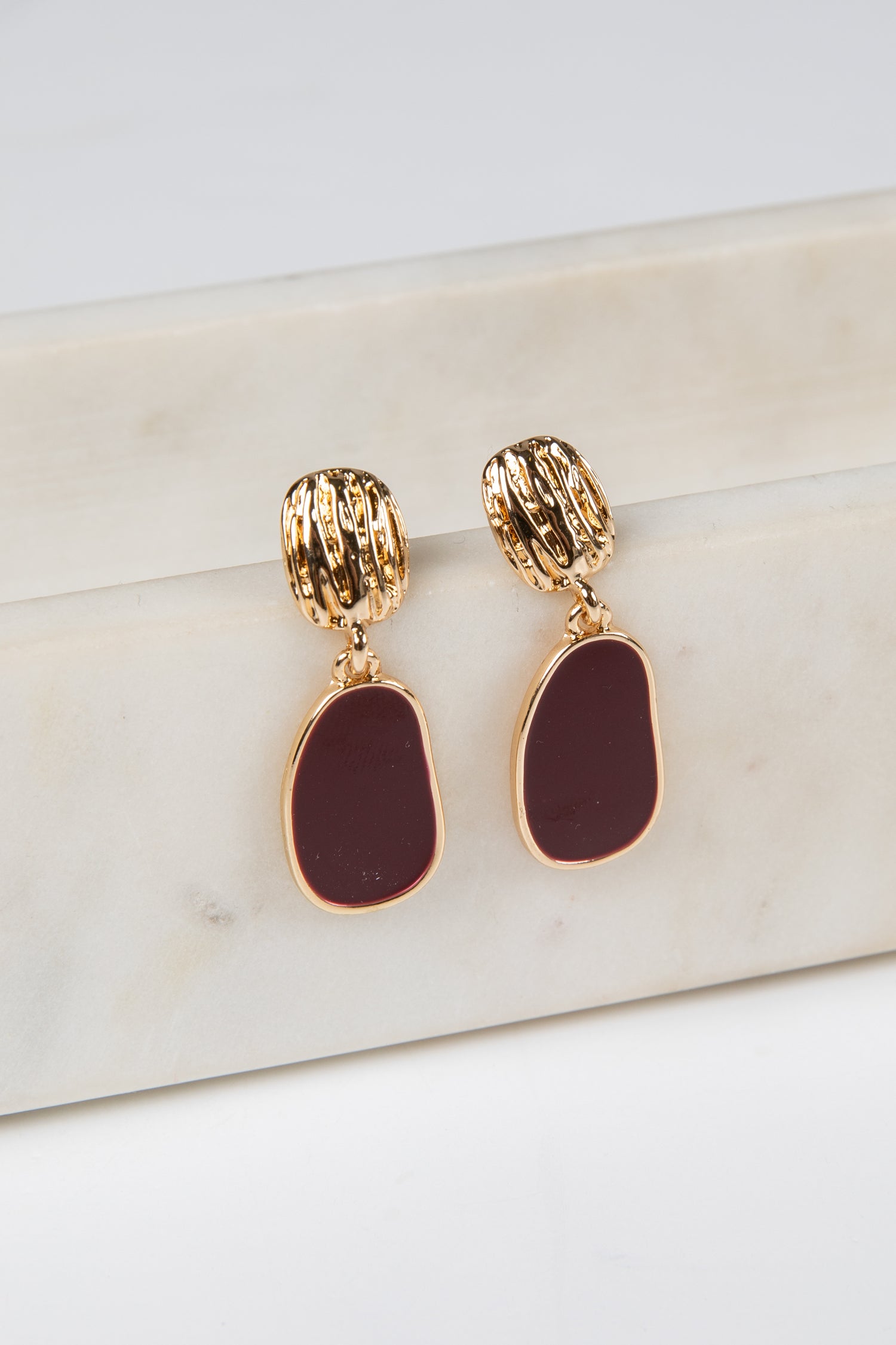 Gold earrings with burgundy stones on a marble surface