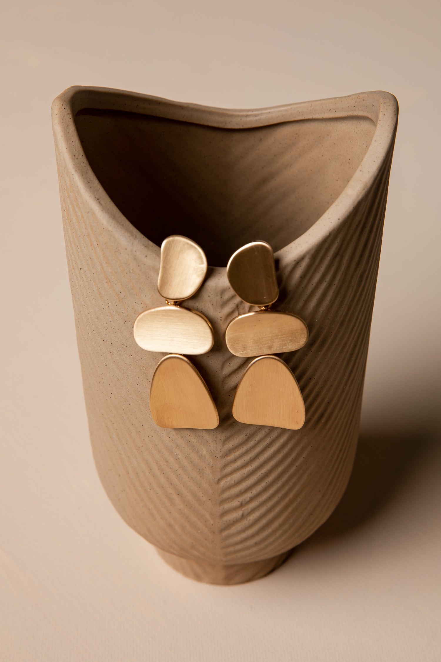 Gold earrings displayed on a textured beige stand against a matching background