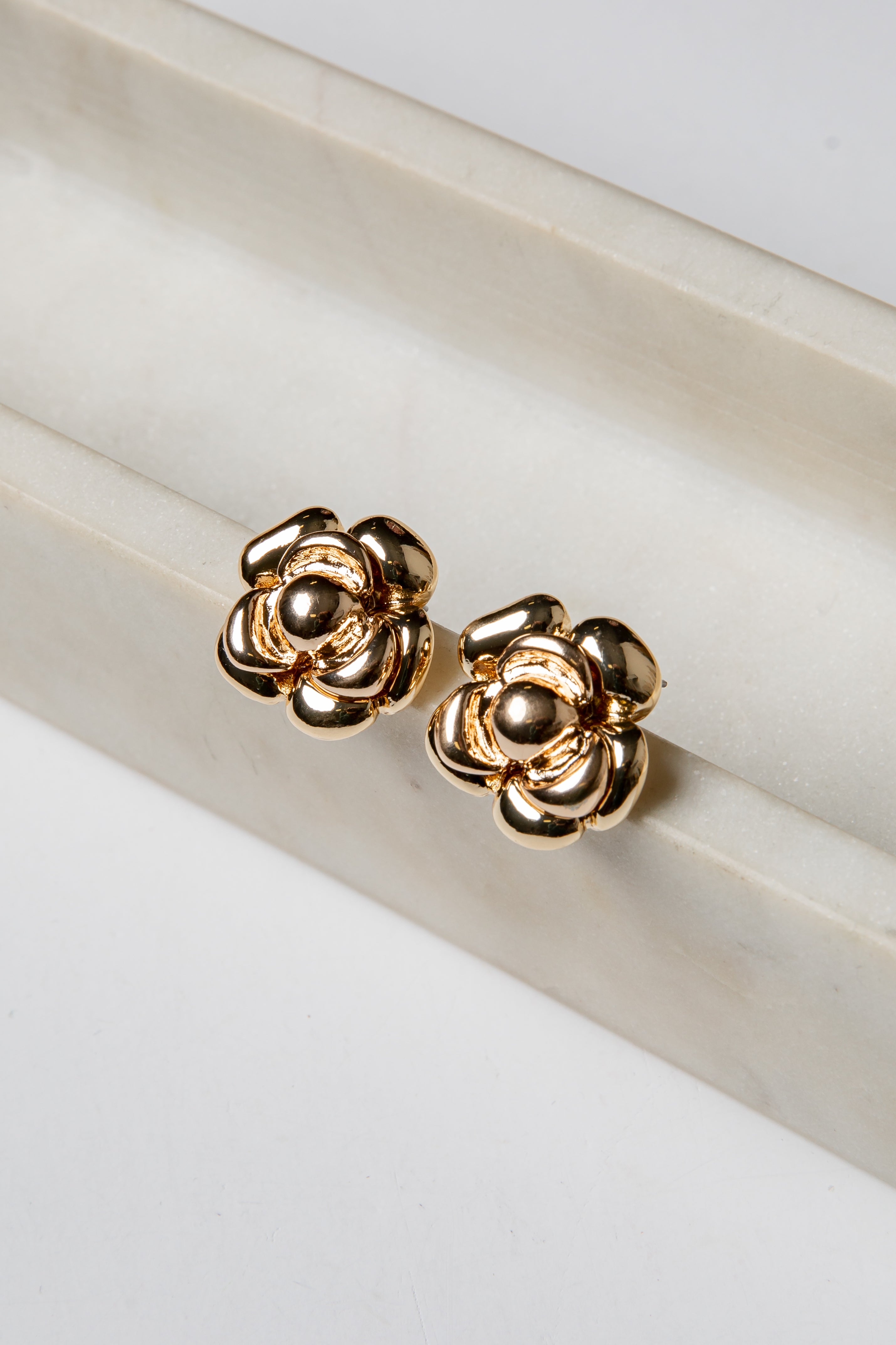 Gold flower-shaped earrings on a white surface