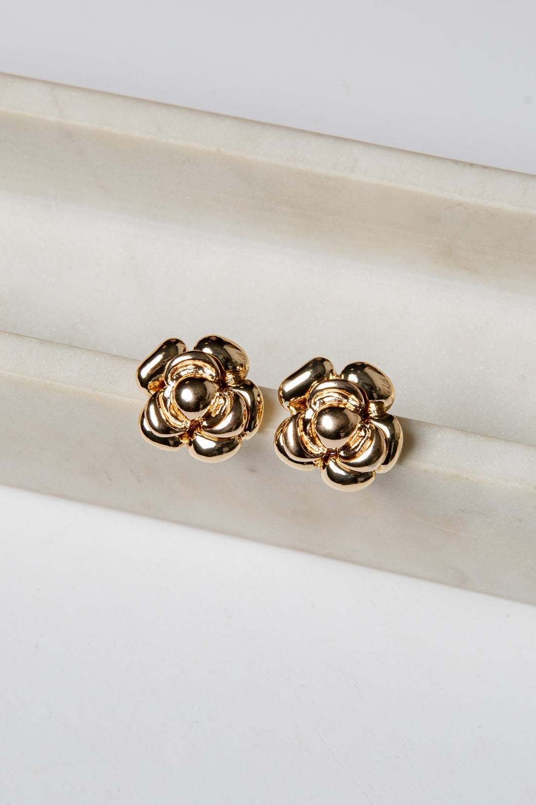Gold flower-shaped earrings on a marble surface