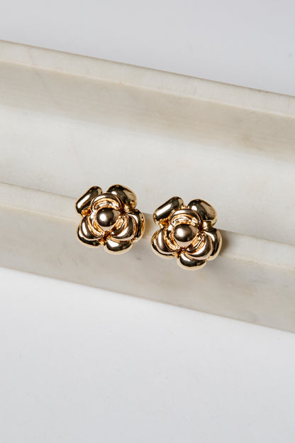 Gold flower-shaped earrings on a marble surface