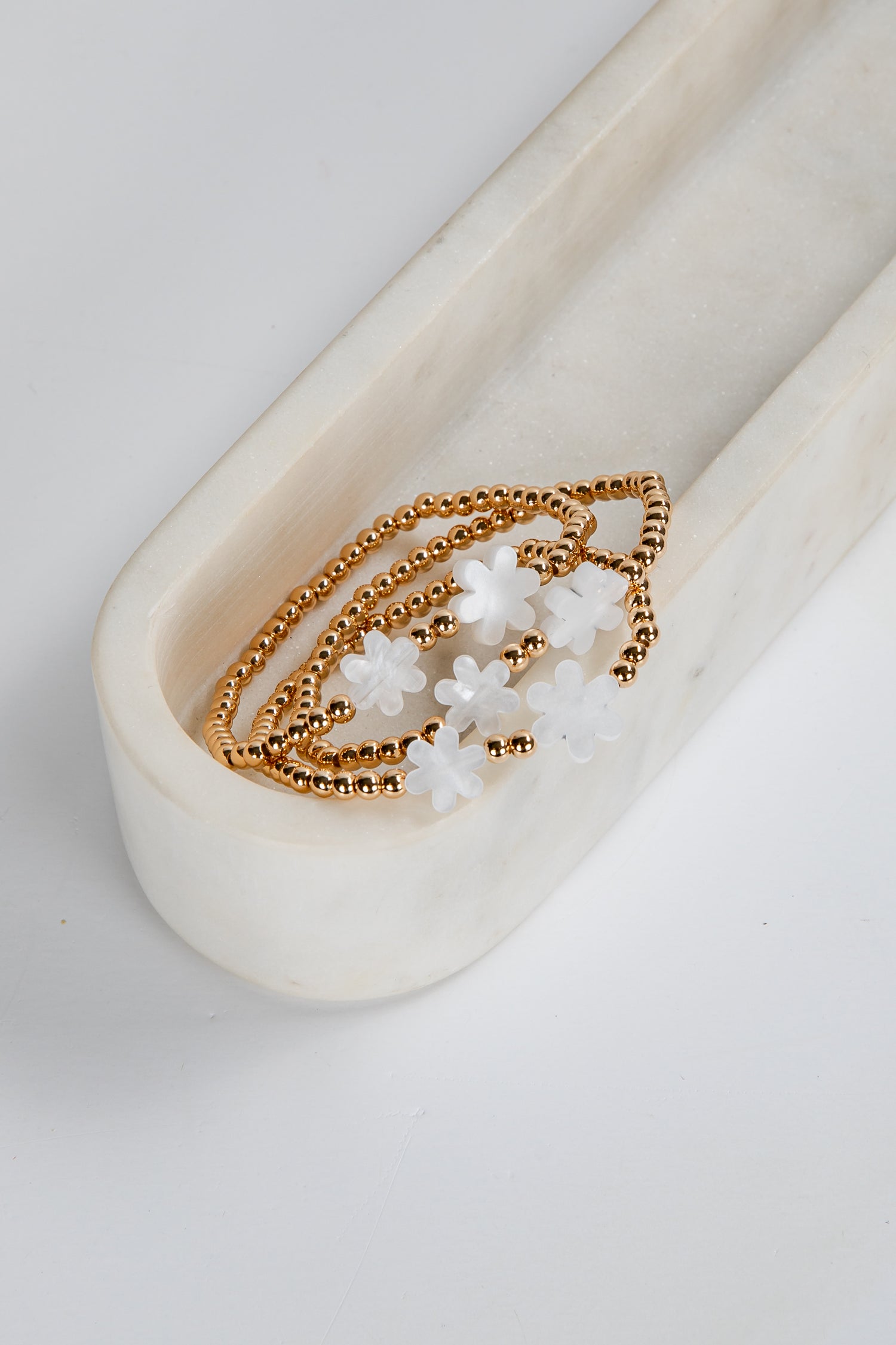Gold bracelet with white beads on a white ceramic dish