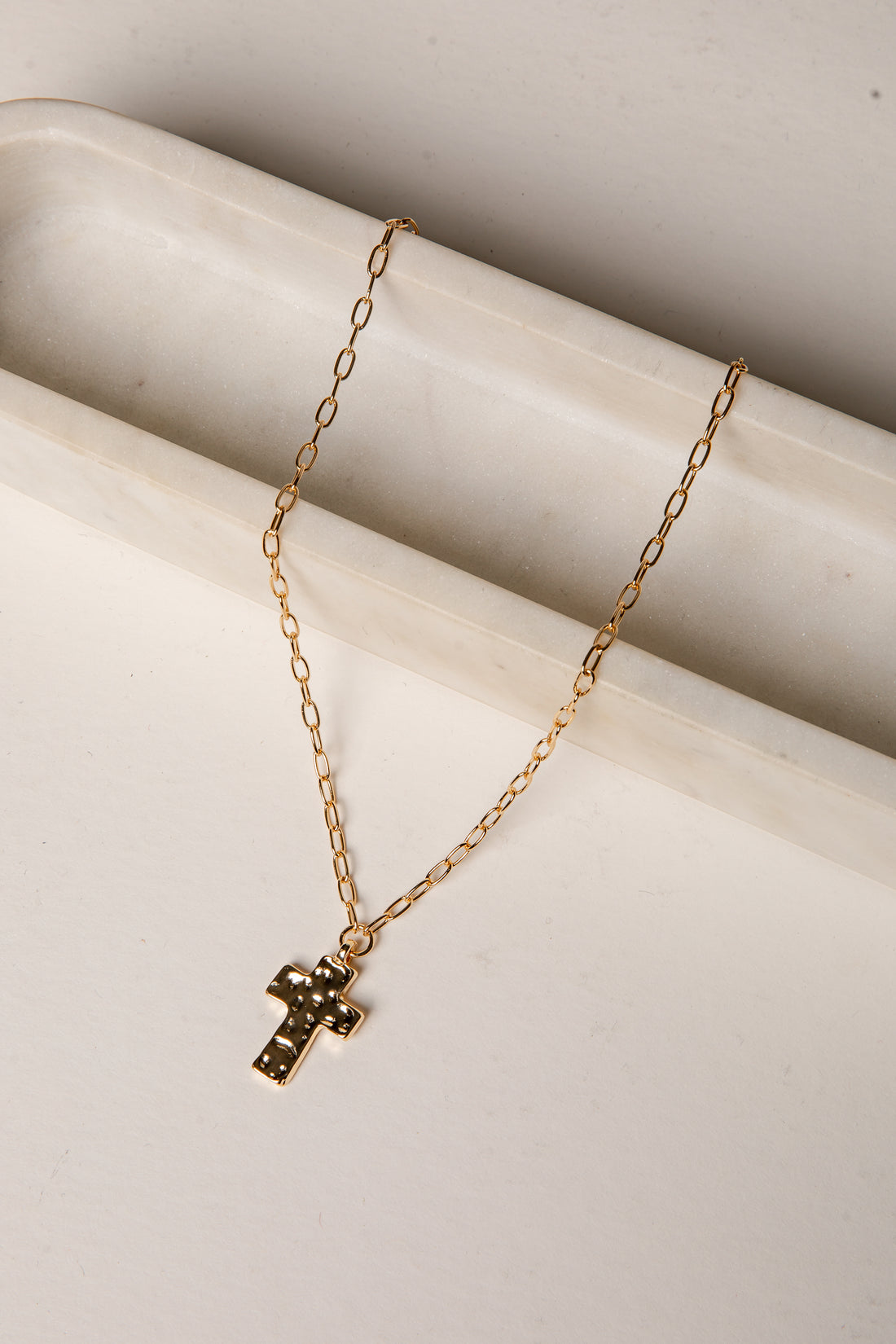 Gold necklace with a cross pendant on a light beige surface