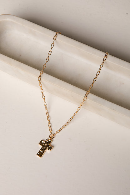 Gold necklace with a cross pendant on a light beige surface