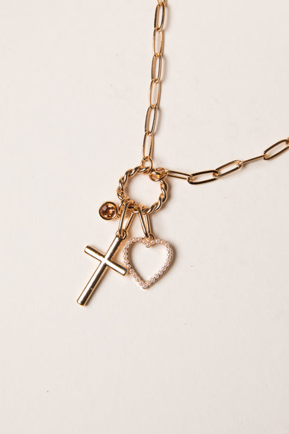 Gold necklace with cross and heart charms on a light background