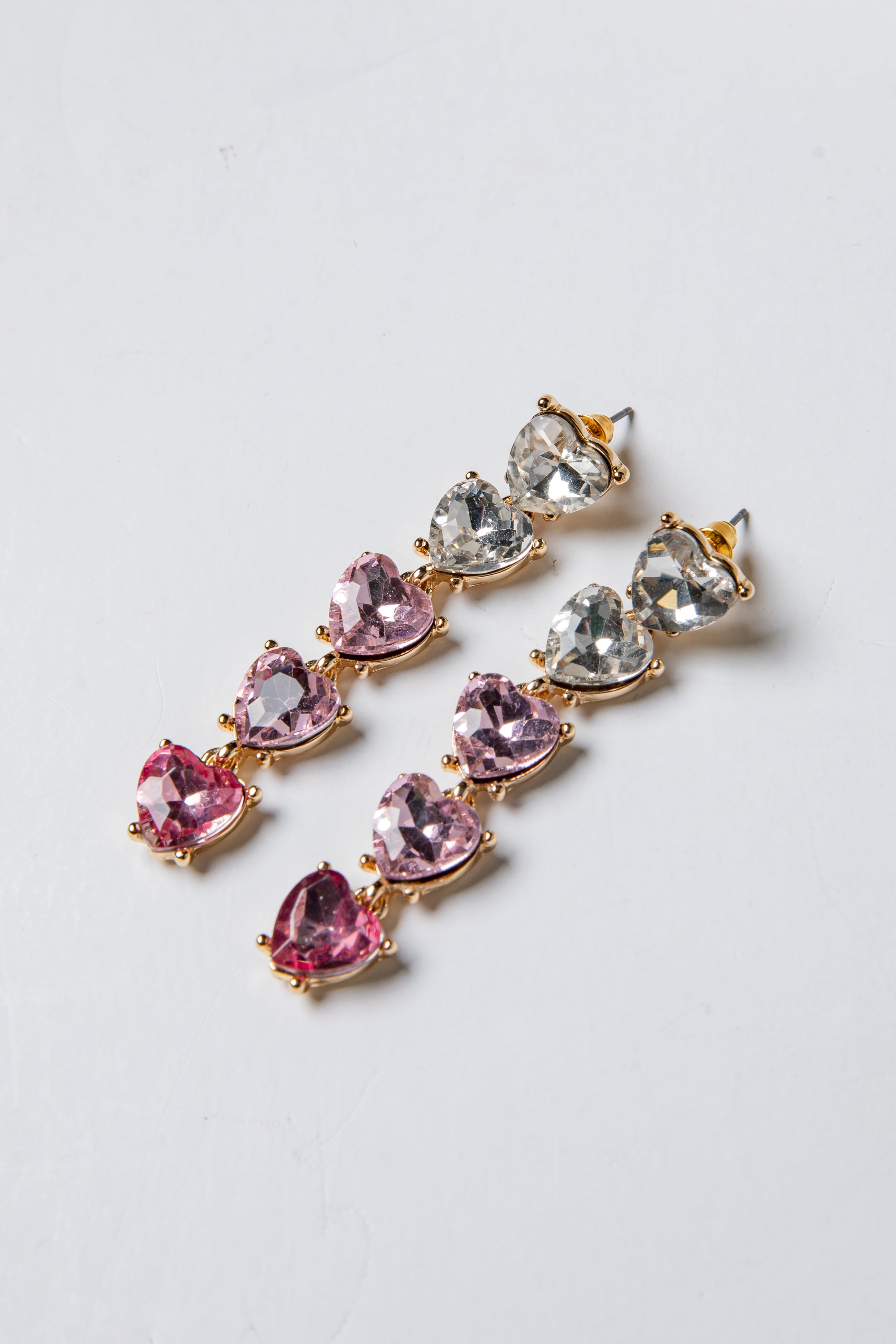 Pair of earrings with pink and clear gemstones on a light gray background