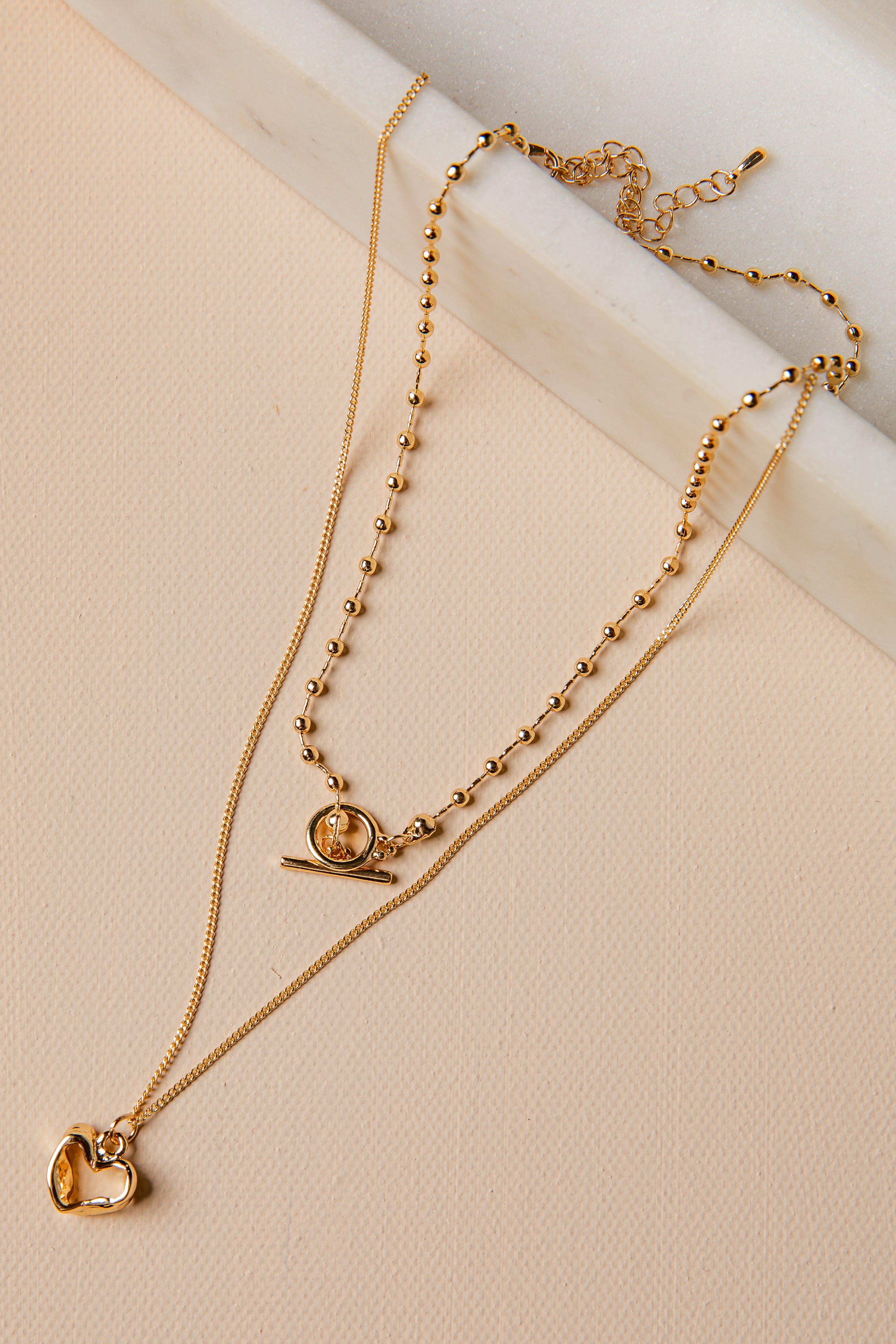 Two gold necklaces with heart and circular pendants on a beige surface