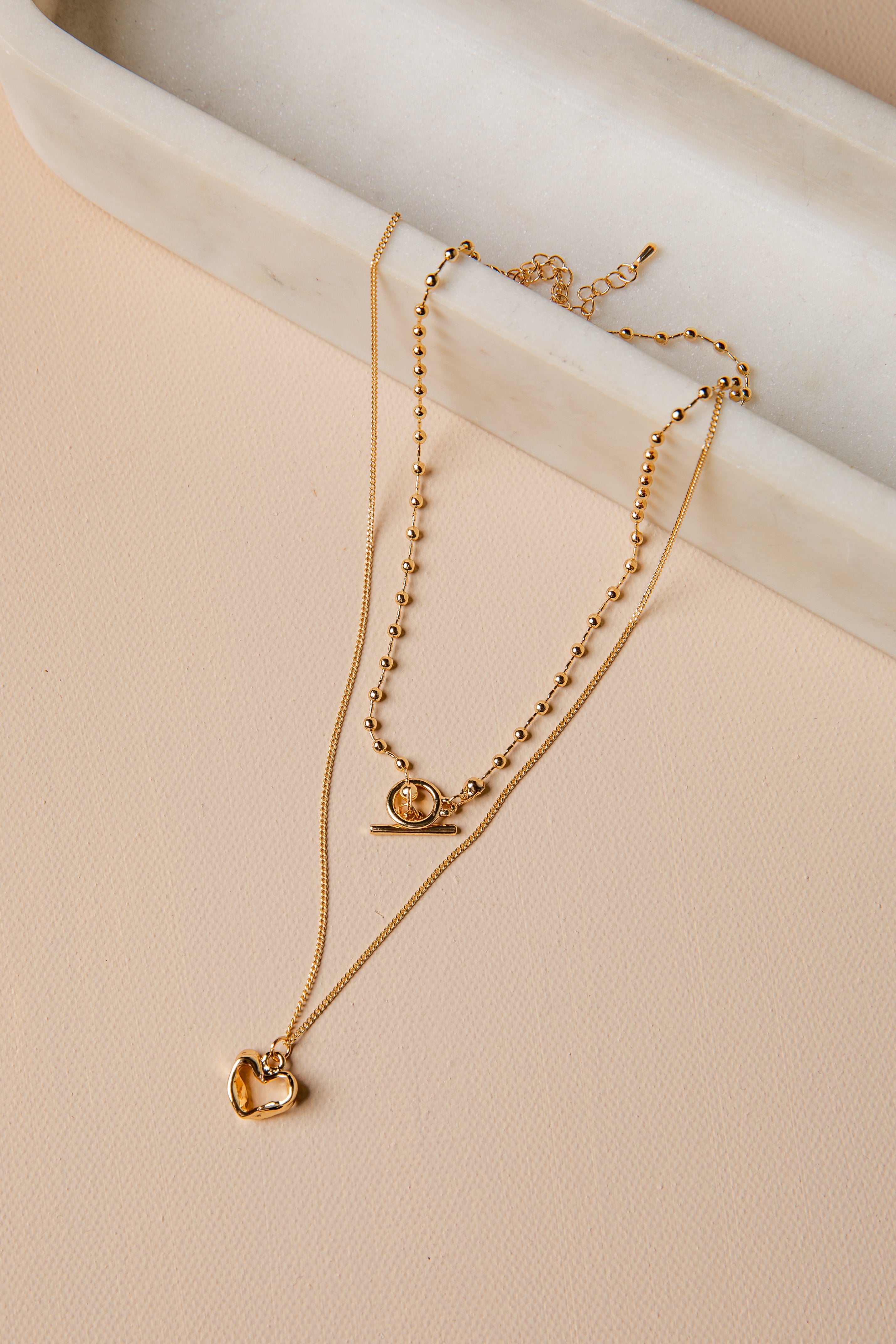 Gold necklace with heart pendant on a beige surface