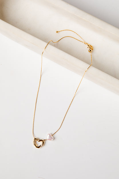 Gold necklace with a heart-shaped clasp and pearl pendant on a white surface