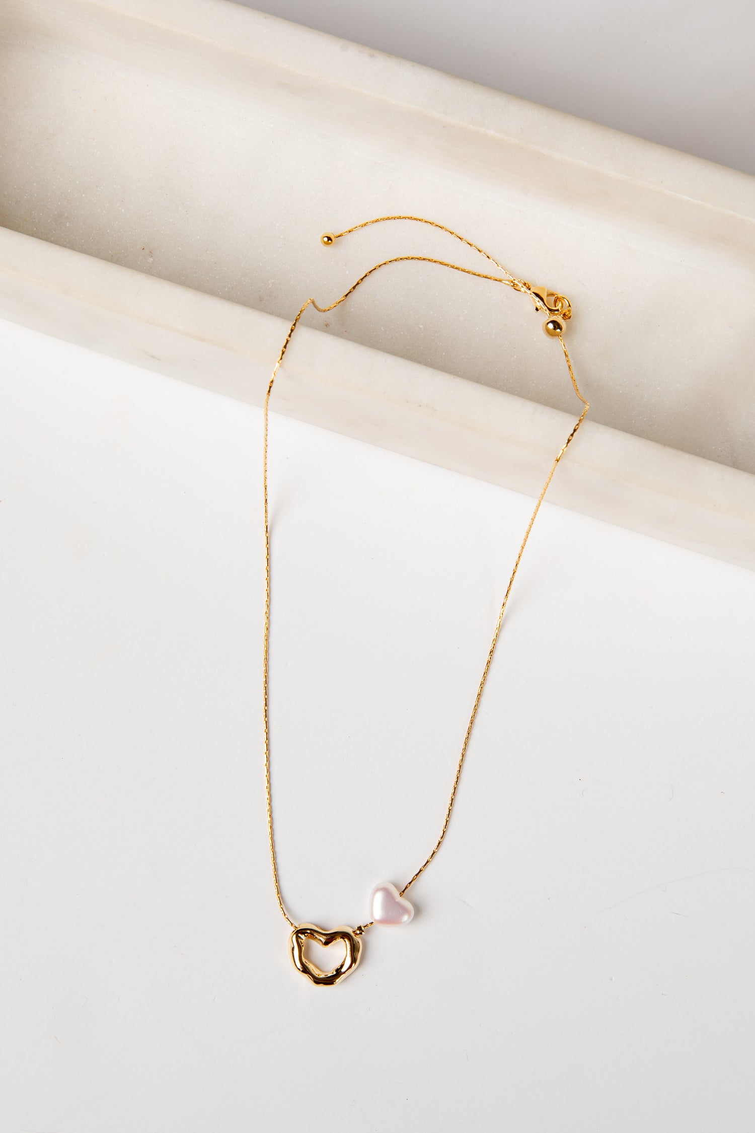 Gold necklace with a heart-shaped pendant on a white surface