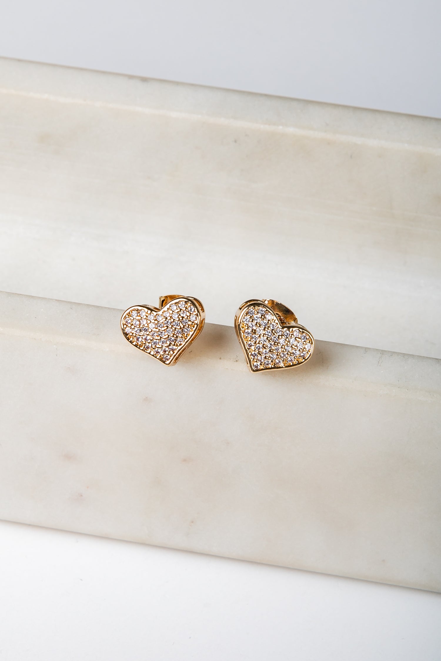 Heart-shaped earrings with embedded stones on a marble surface