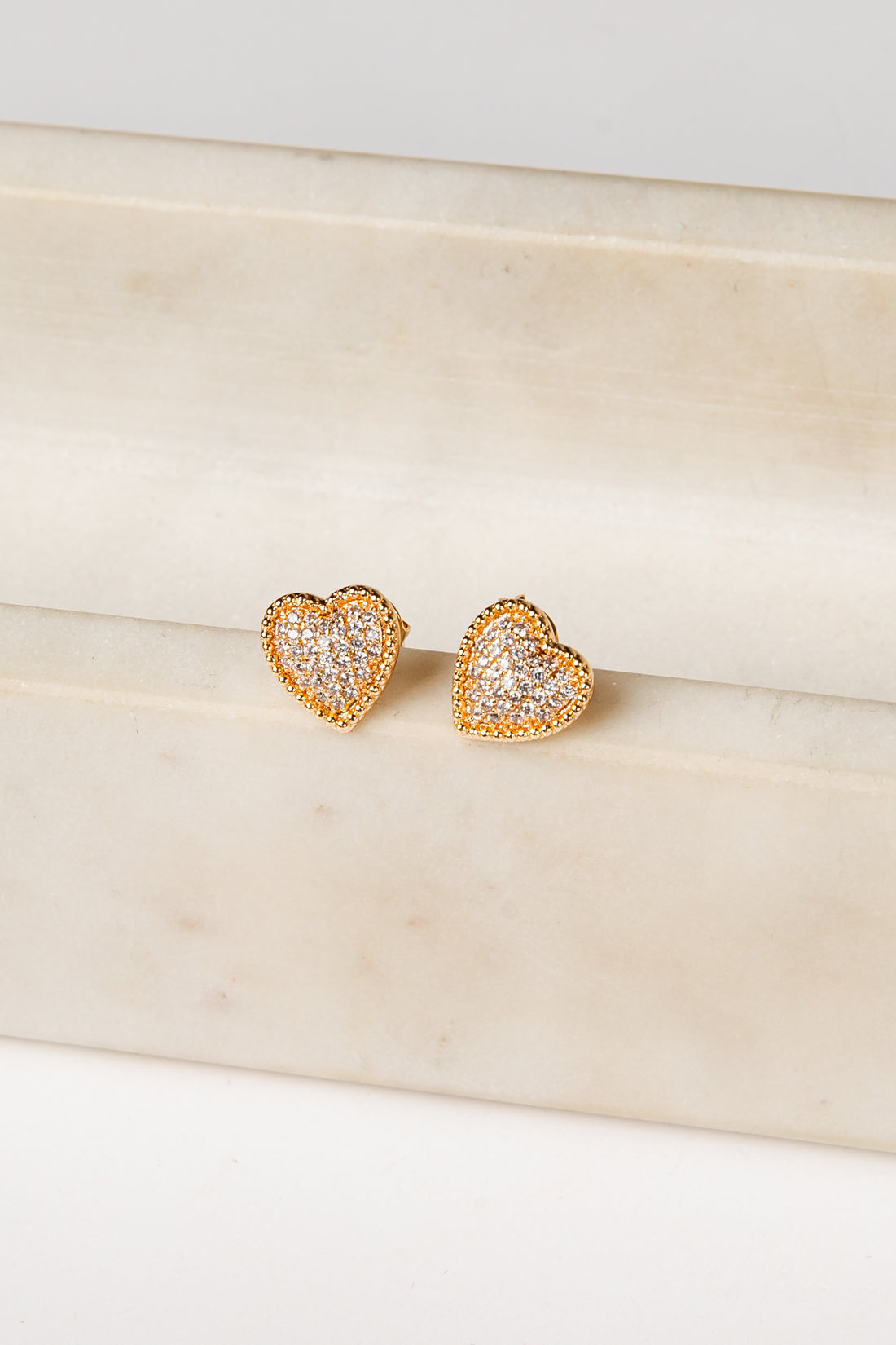 Heart-shaped gold earrings on a beige marble surface