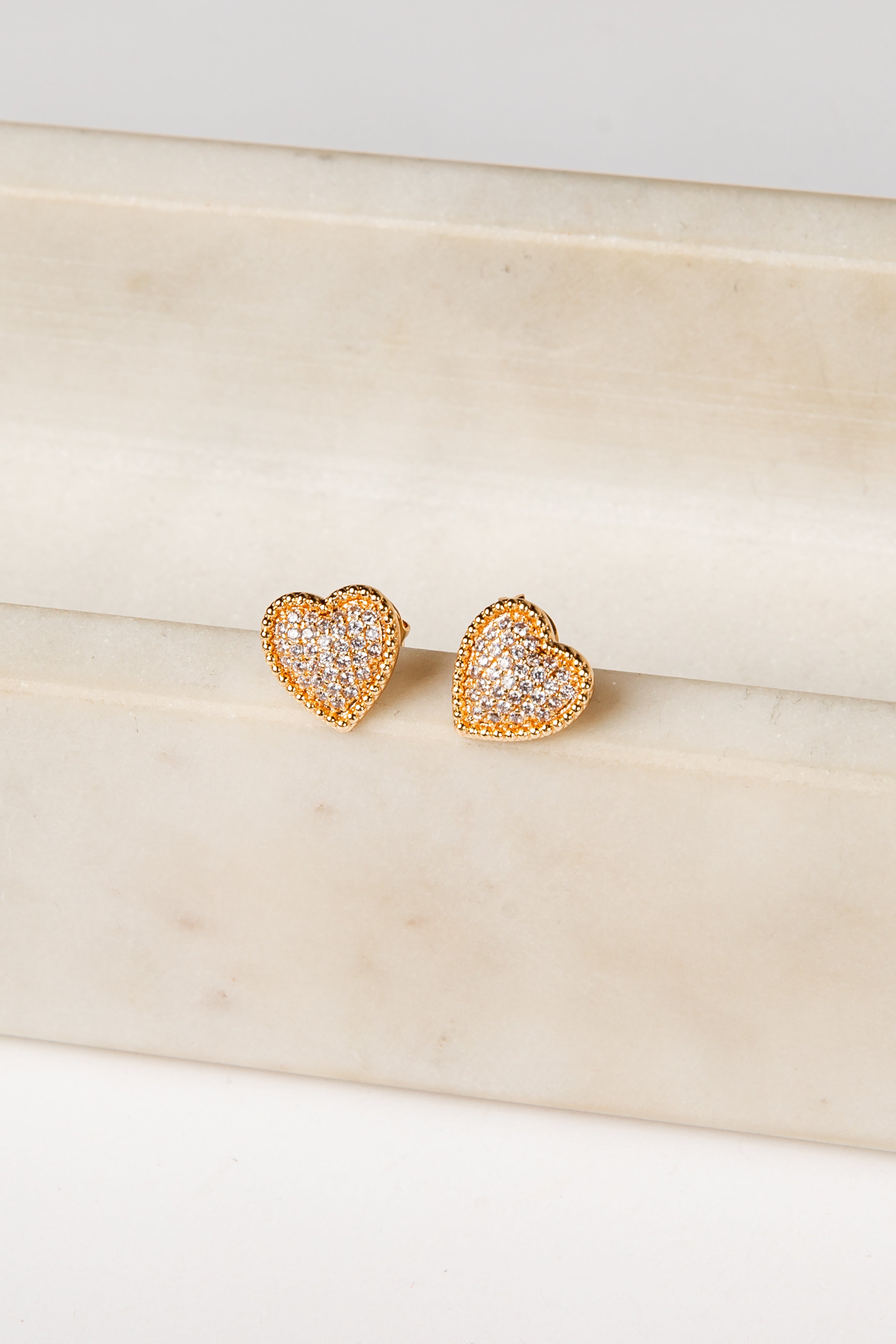 Heart-shaped gold earrings on a beige marble surface
