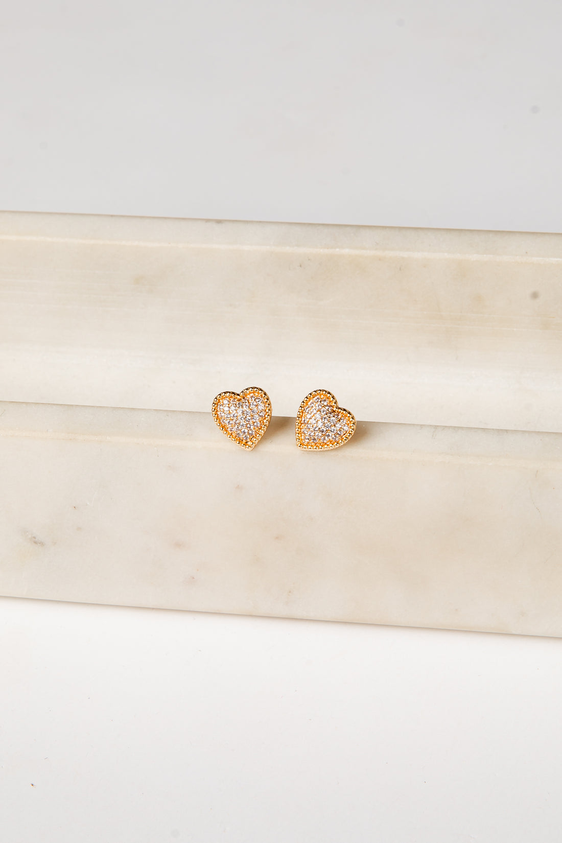 Heart-shaped earrings with clear stones on a light wooden surface